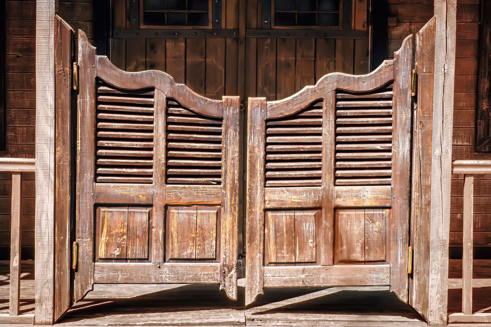 A pair of wooden saloon doors are open in front of a wooden building.