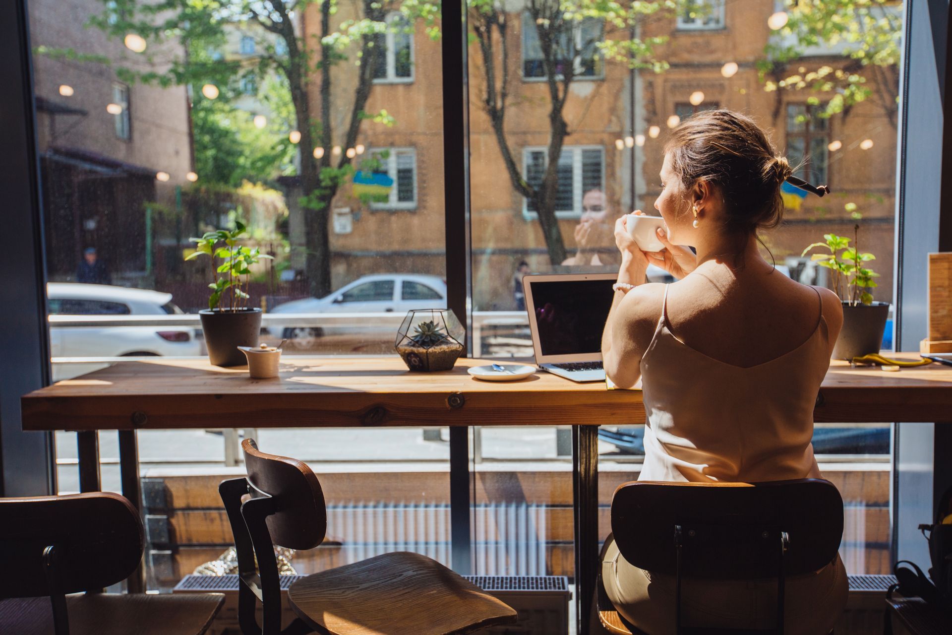 A woman is sitting at a table with a laptop and drinking coffee.