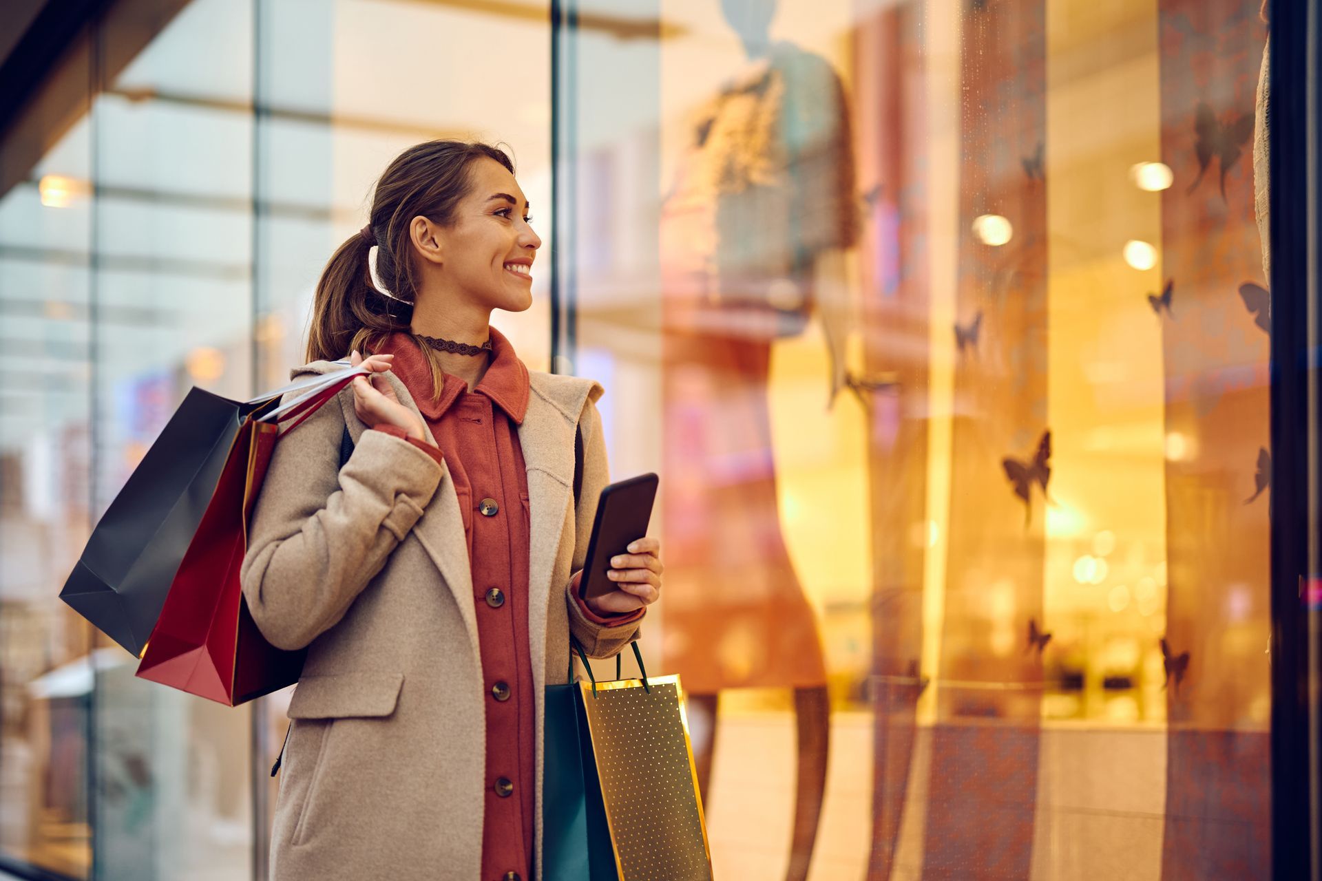 A woman is holding shopping bags and looking at a store window.