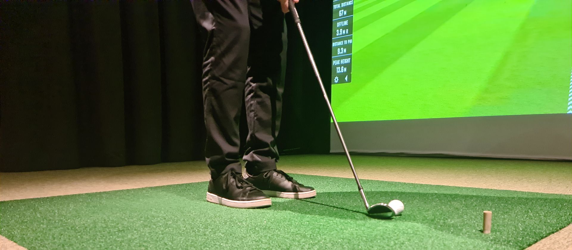 A man is standing on a green mat holding a golf club.