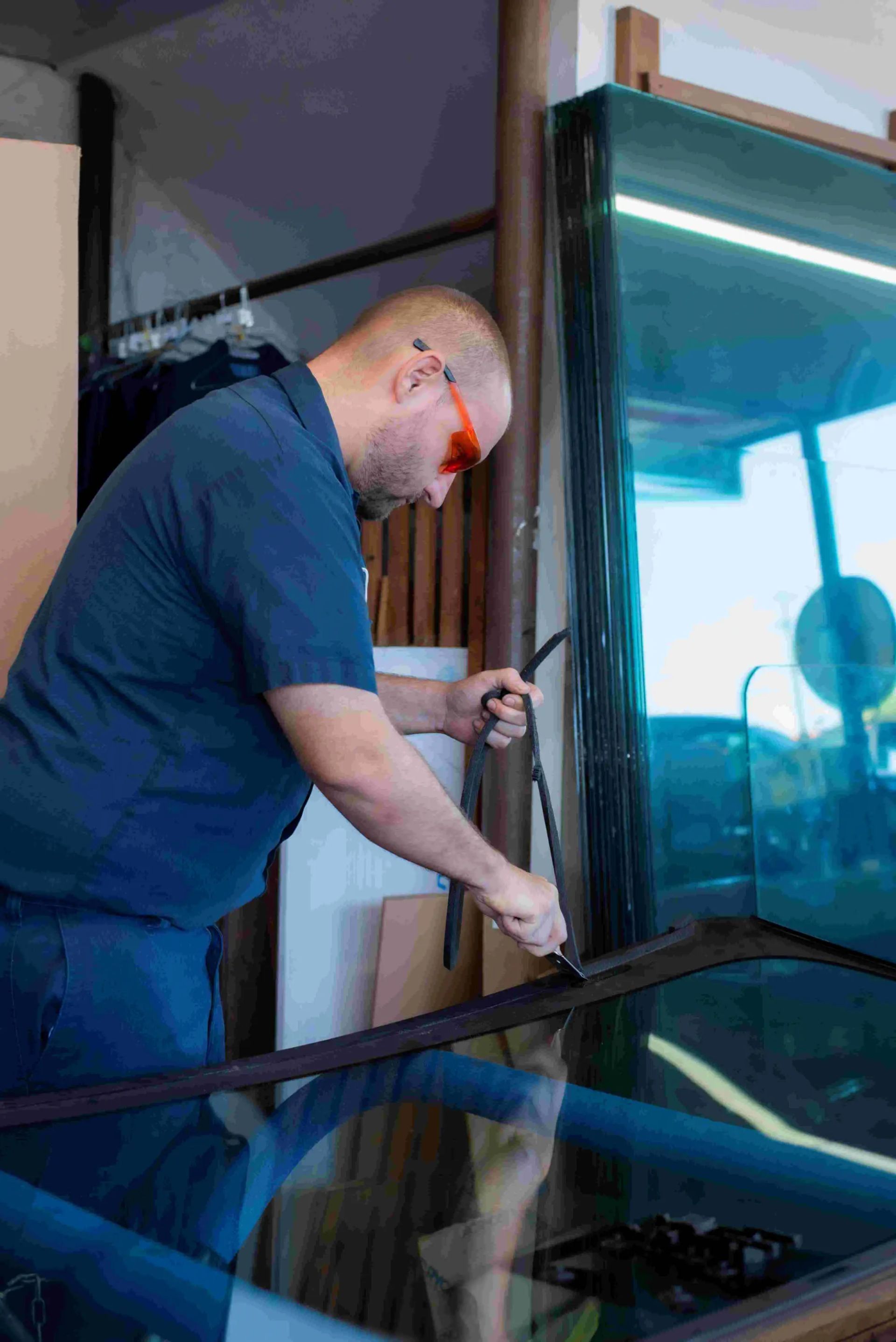 A man wearing safety glasses working on glass. He uses a tool in a workshop.