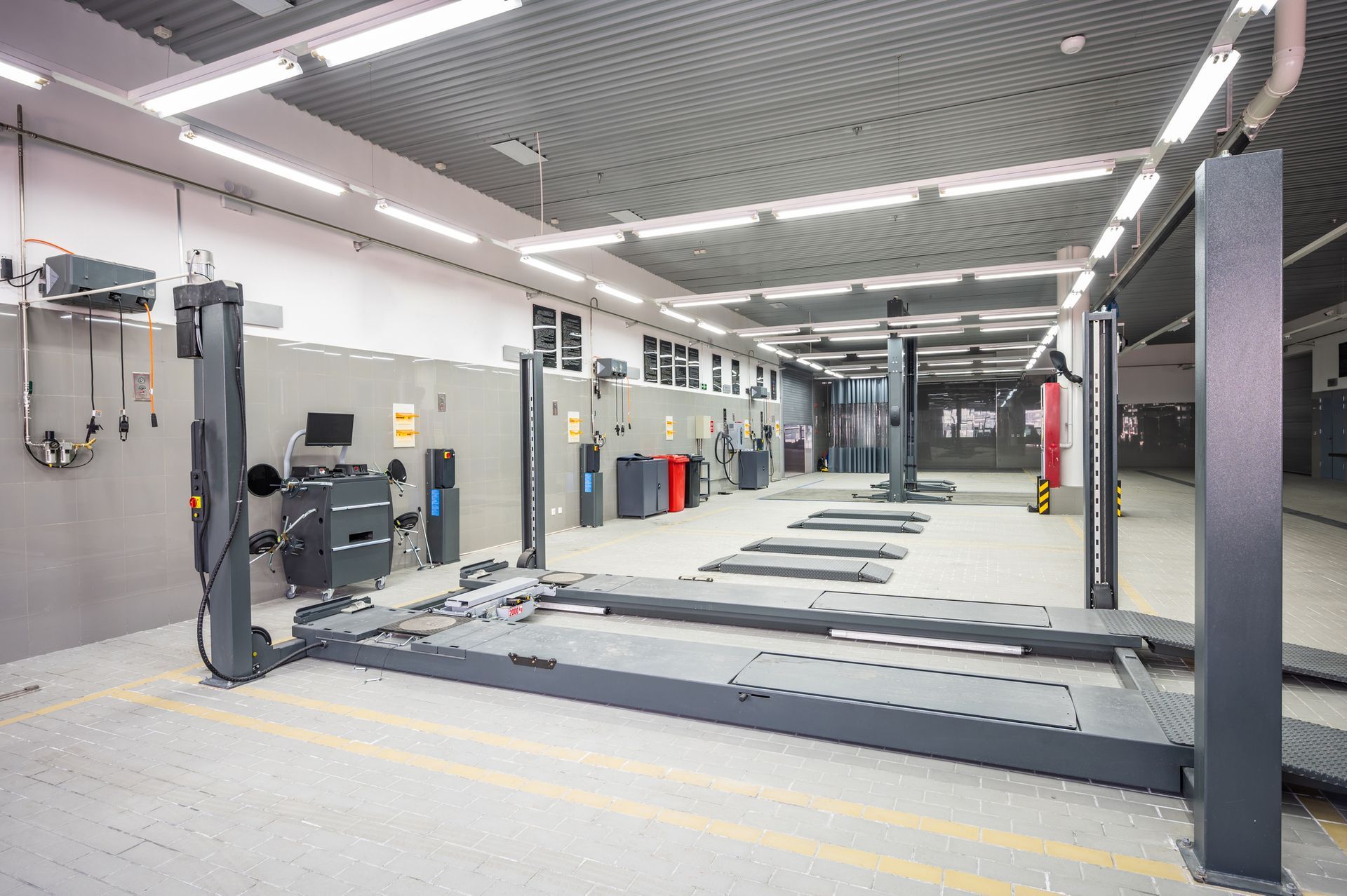 Automotive workshop interior with vehicle lifts, tools, and lighting fixtures.