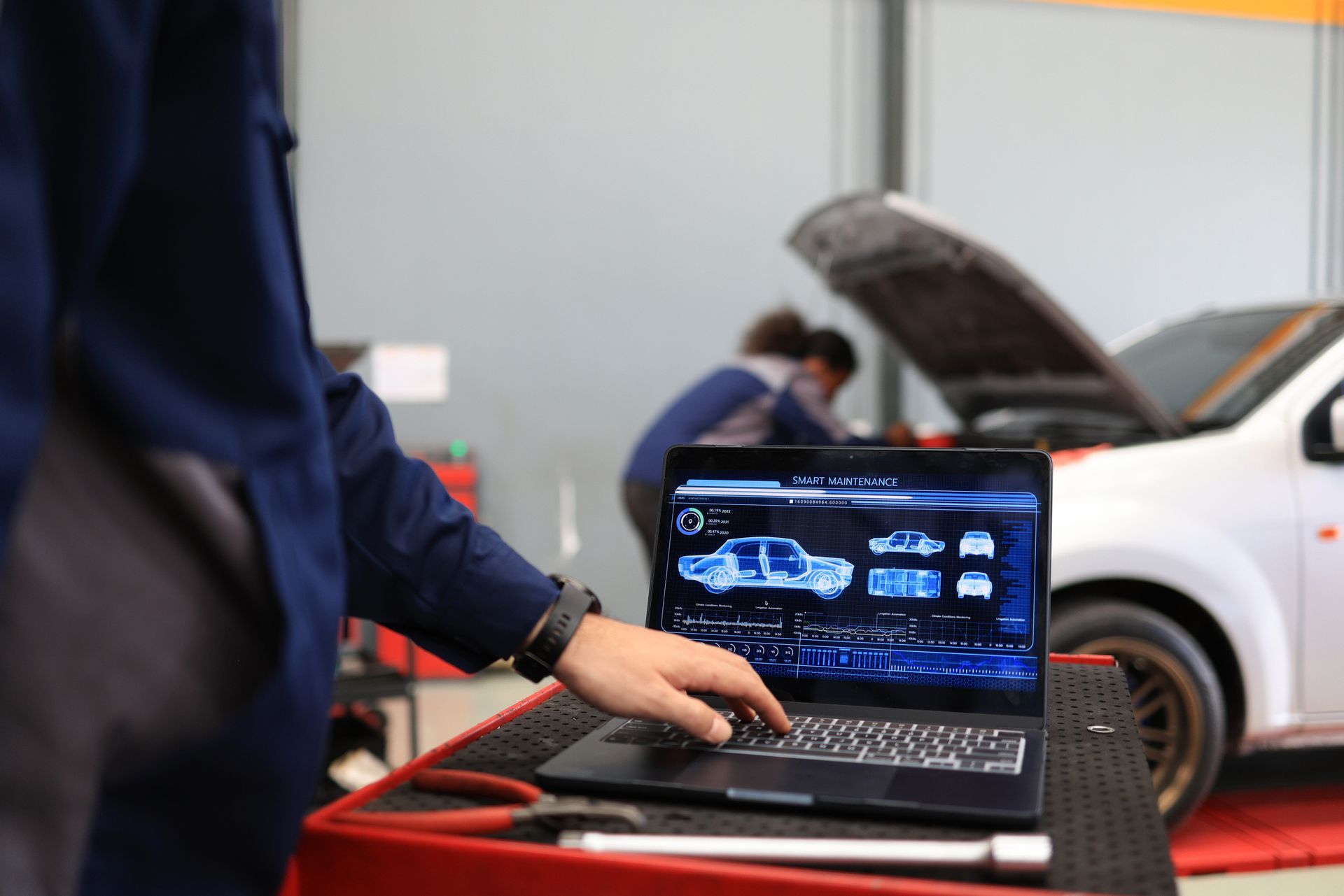 Mechanic using a laptop for car diagnostics in a repair shop. White truck with open hood in background.
