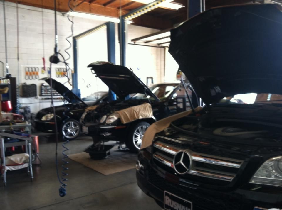Three cars with open hoods in a garage, lights, tools visible. Three cars with open hoods in a garage, lights, tools visible.