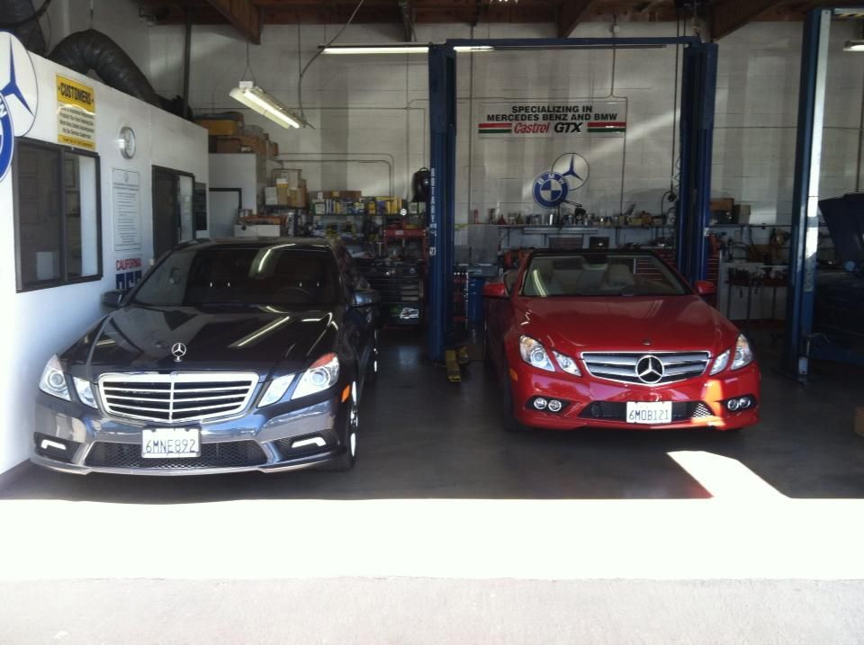 Two Mercedes-Benz cars inside a repair shop; a black sedan and a red convertible. Two Mercedes-Benz cars inside a repair shop; a black sedan and a red convertible.