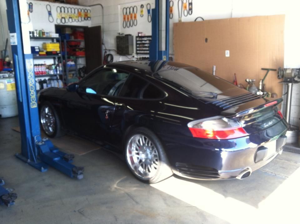 Dark blue Porsche 911 Turbo in a repair shop, on a lift. Silver wheels, tools on the wall. Dark blue Porsche 911 Turbo in a repair shop, on a lift. Silver wheels, tools on the wall.