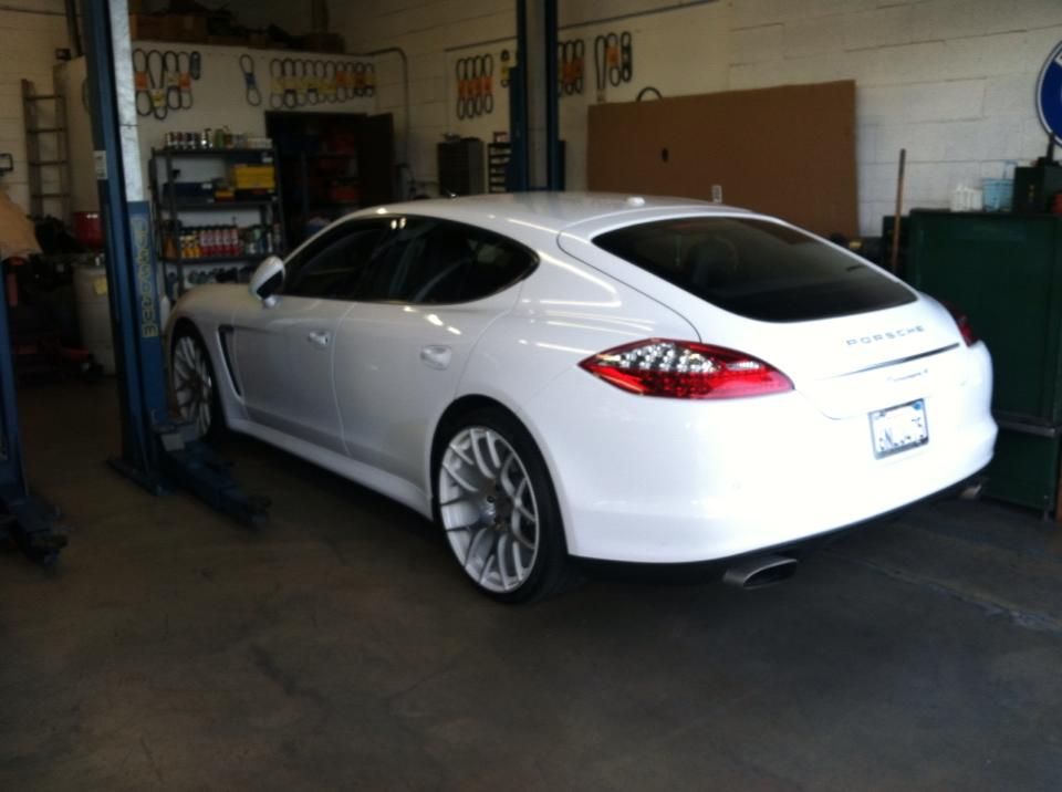 White Porsche Panamera on a car lift in an auto repair shop. White Porsche Panamera on a car lift in an auto repair shop.