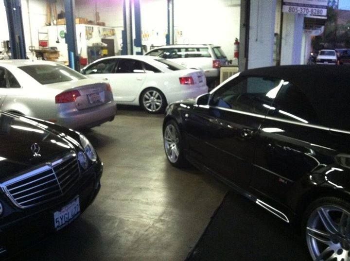 Cars inside a repair shop. A black convertible, silver and white sedans, and a white wagon are visible. Cars inside a repair shop. A black convertible, silver and white sedans, and a white wagon are visible.