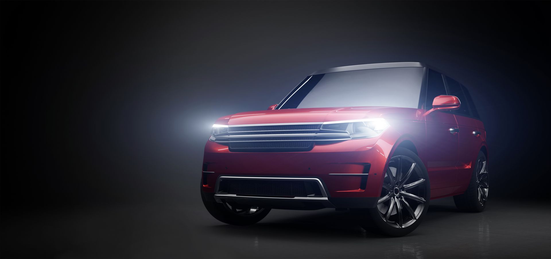 Red SUV with headlights on in a dark studio.