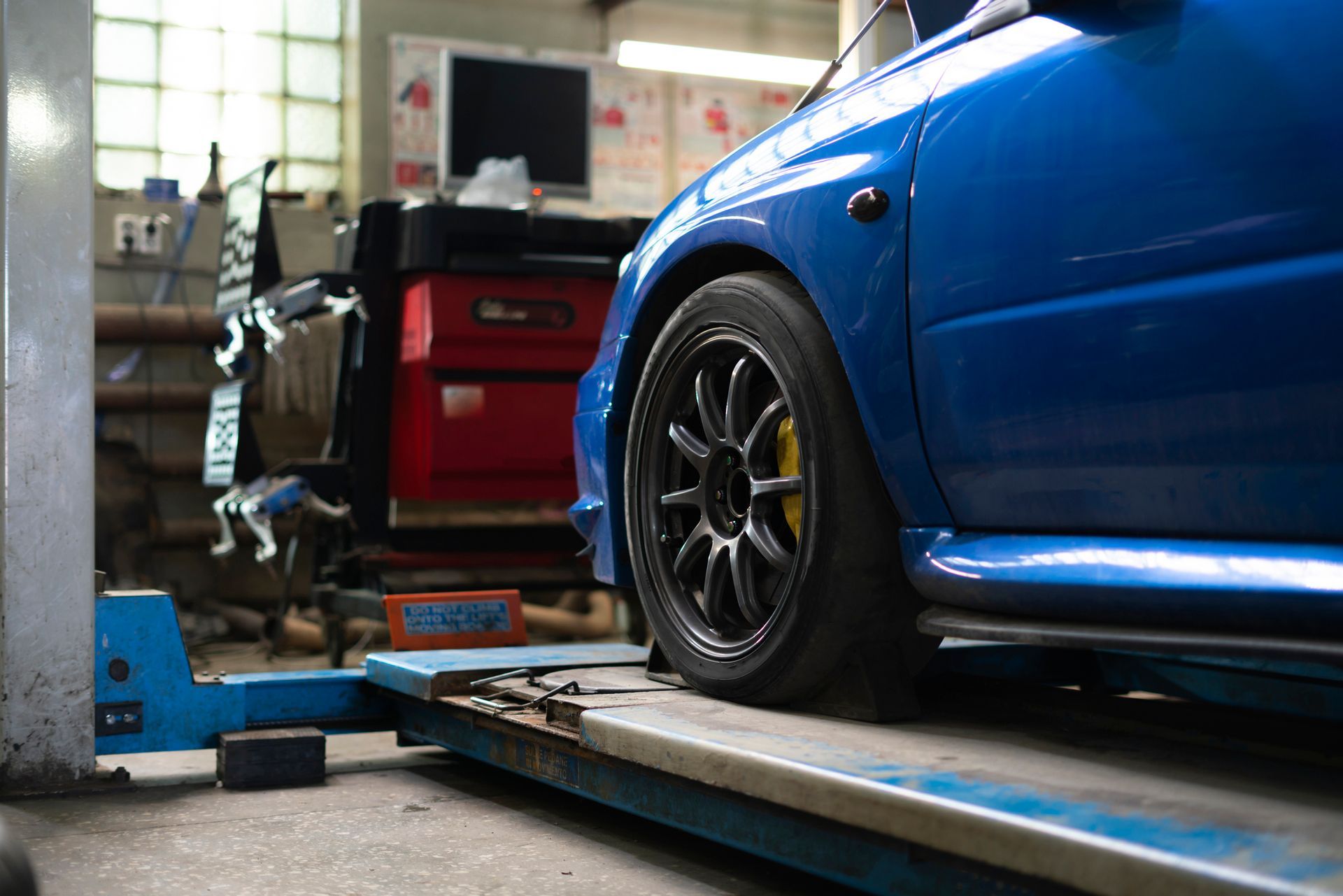 Blue car raised on a lift in a garage, black wheels, yellow calipers.