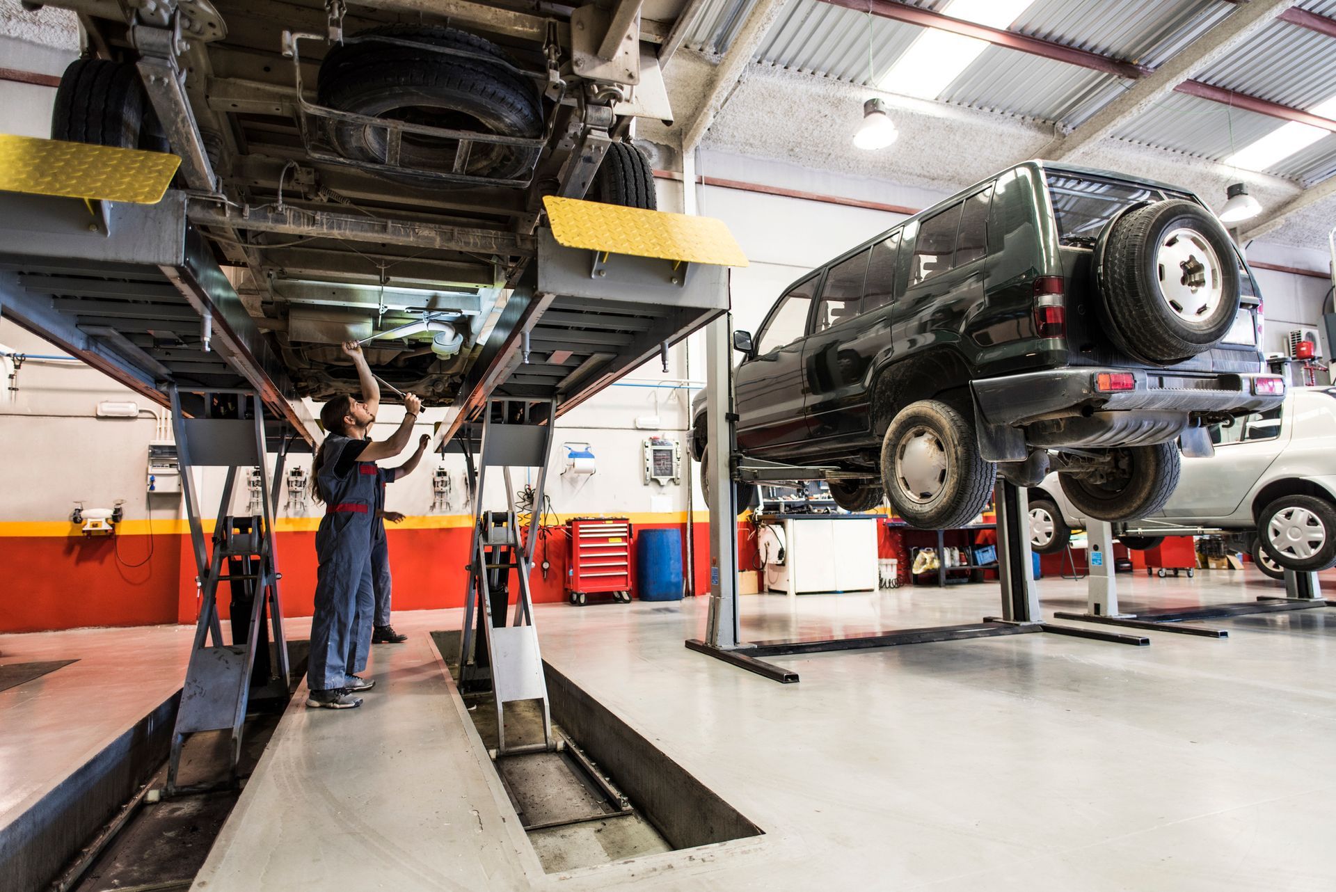 Mechanics working on cars lifted on hoists in an auto repair shop.