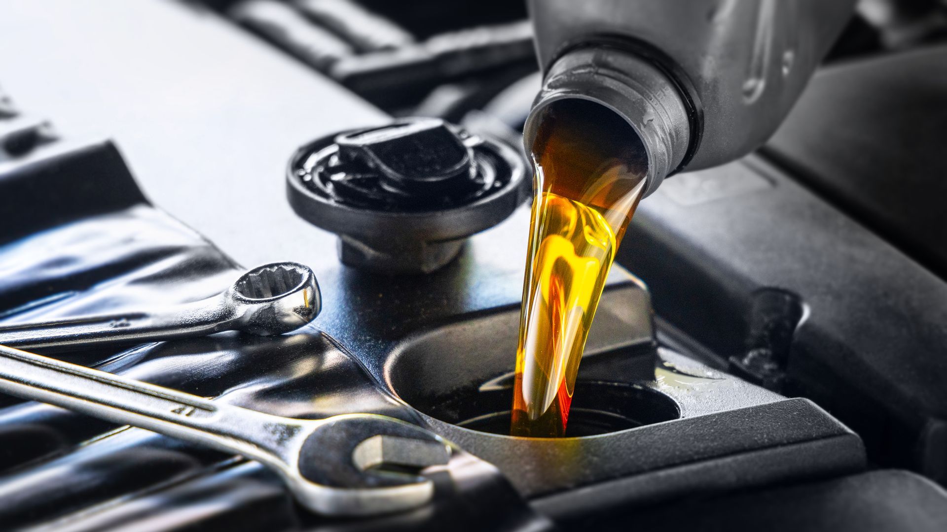 Pouring oil into a car engine, with wrenches nearby.