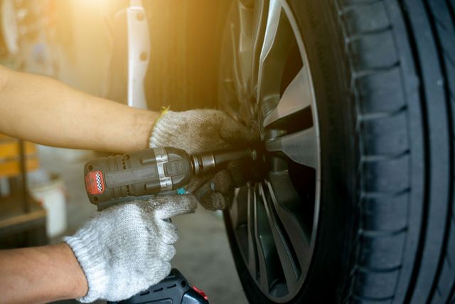 Hands with work gloves using a power tool to remove lug nuts from a car tire.