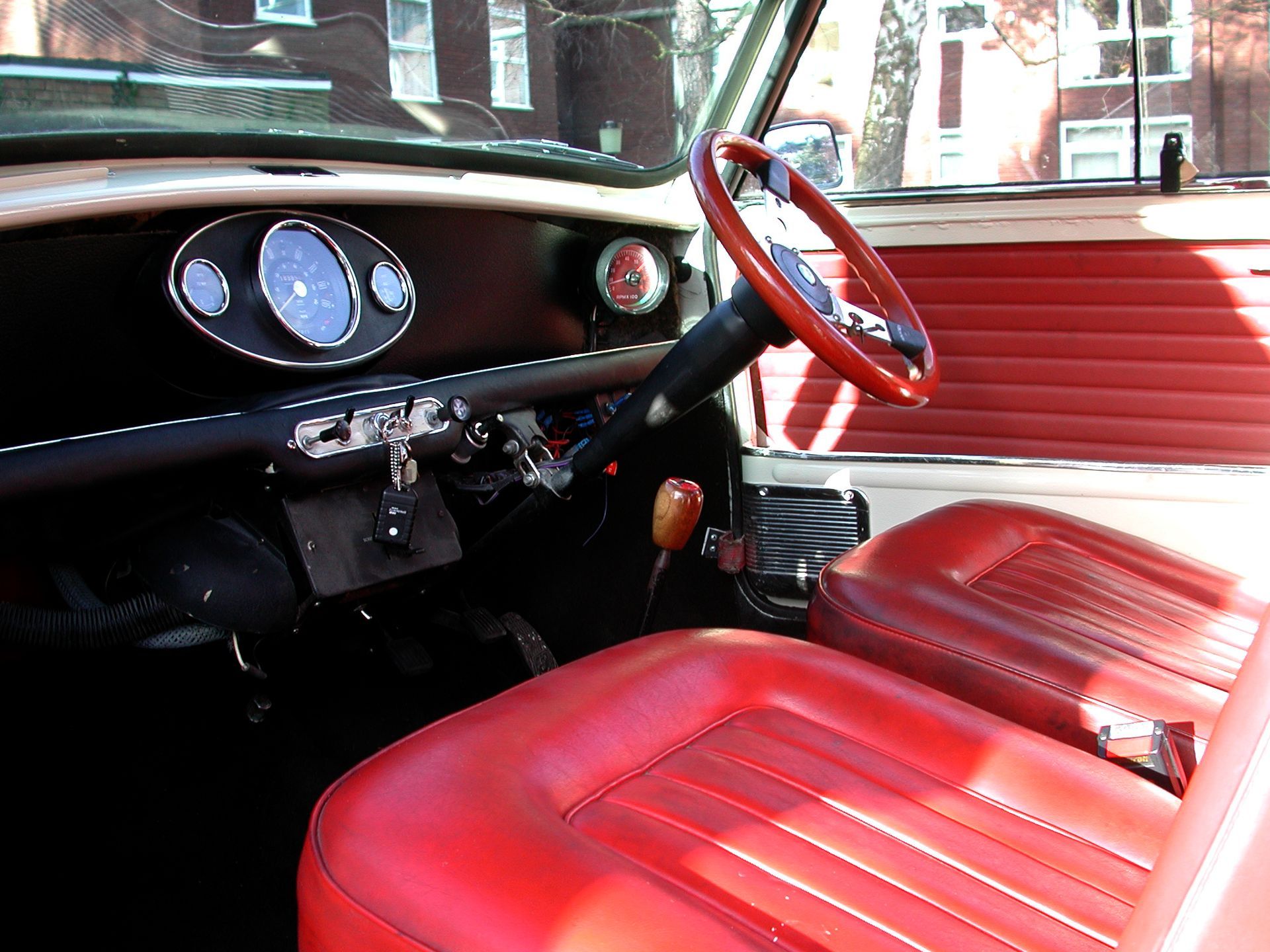 Interior of a classic Mini Cooper with red seats and steering wheel, black dashboard, and gauges.