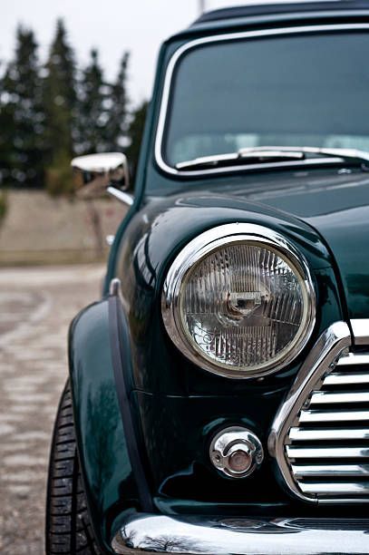 Dark green classic Mini Cooper car, front view, with a chrome headlight and grille.