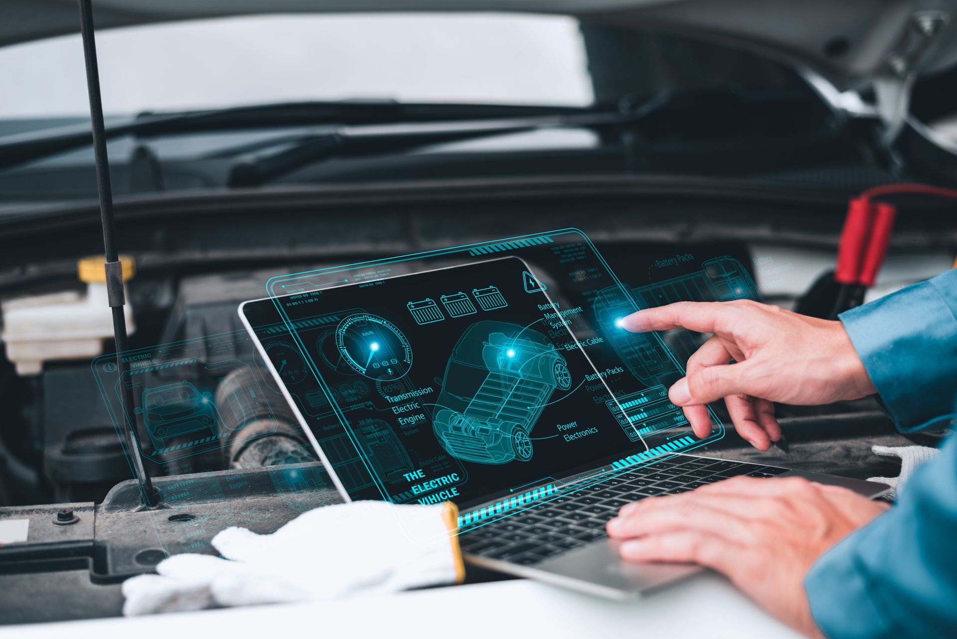 Mechanic uses a laptop with diagnostic software under a car hood. Blue-lit screen displays engine data.