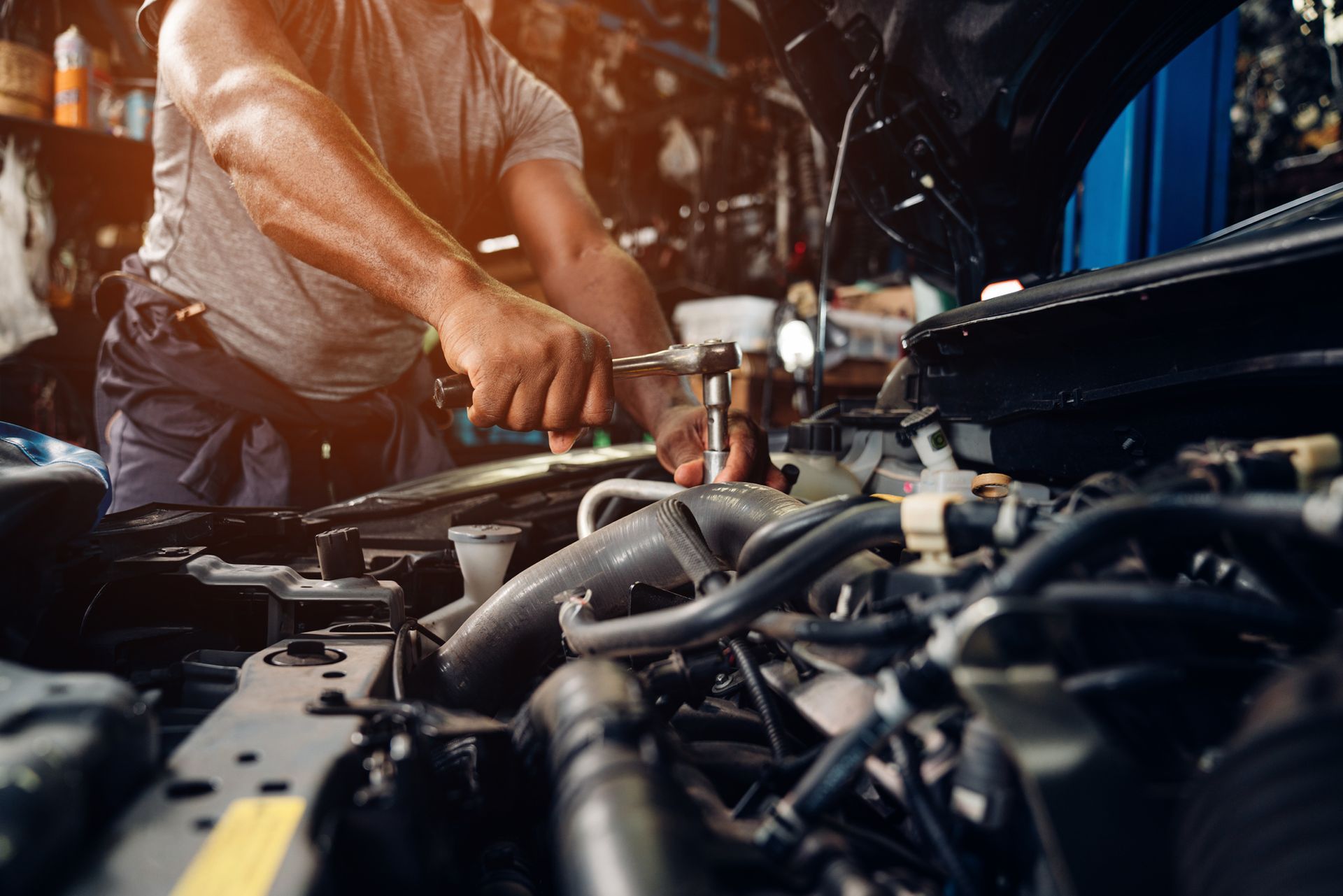 Mechanic working on car engine in a garage; using a wrench.