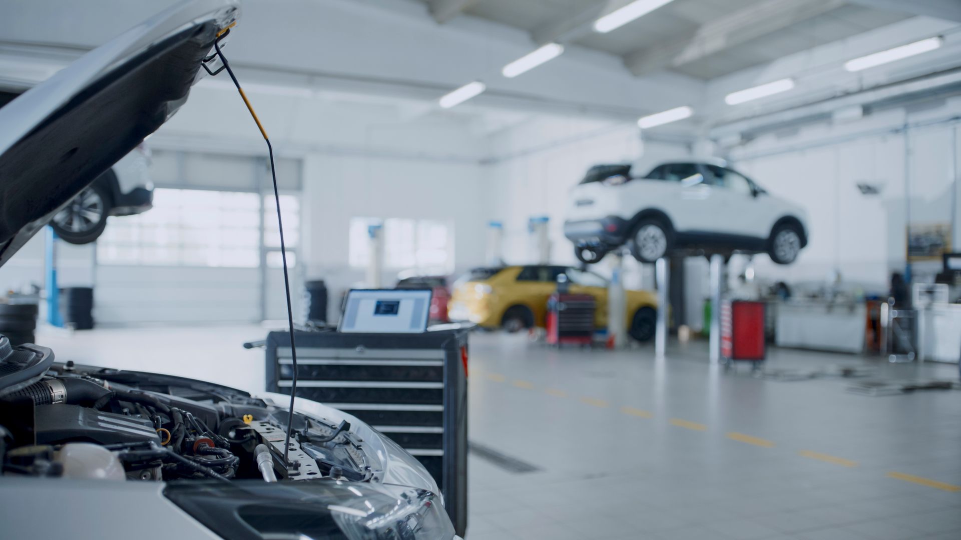 Car in a repair shop with hood open, diagnostic tools, and cars on lifts.