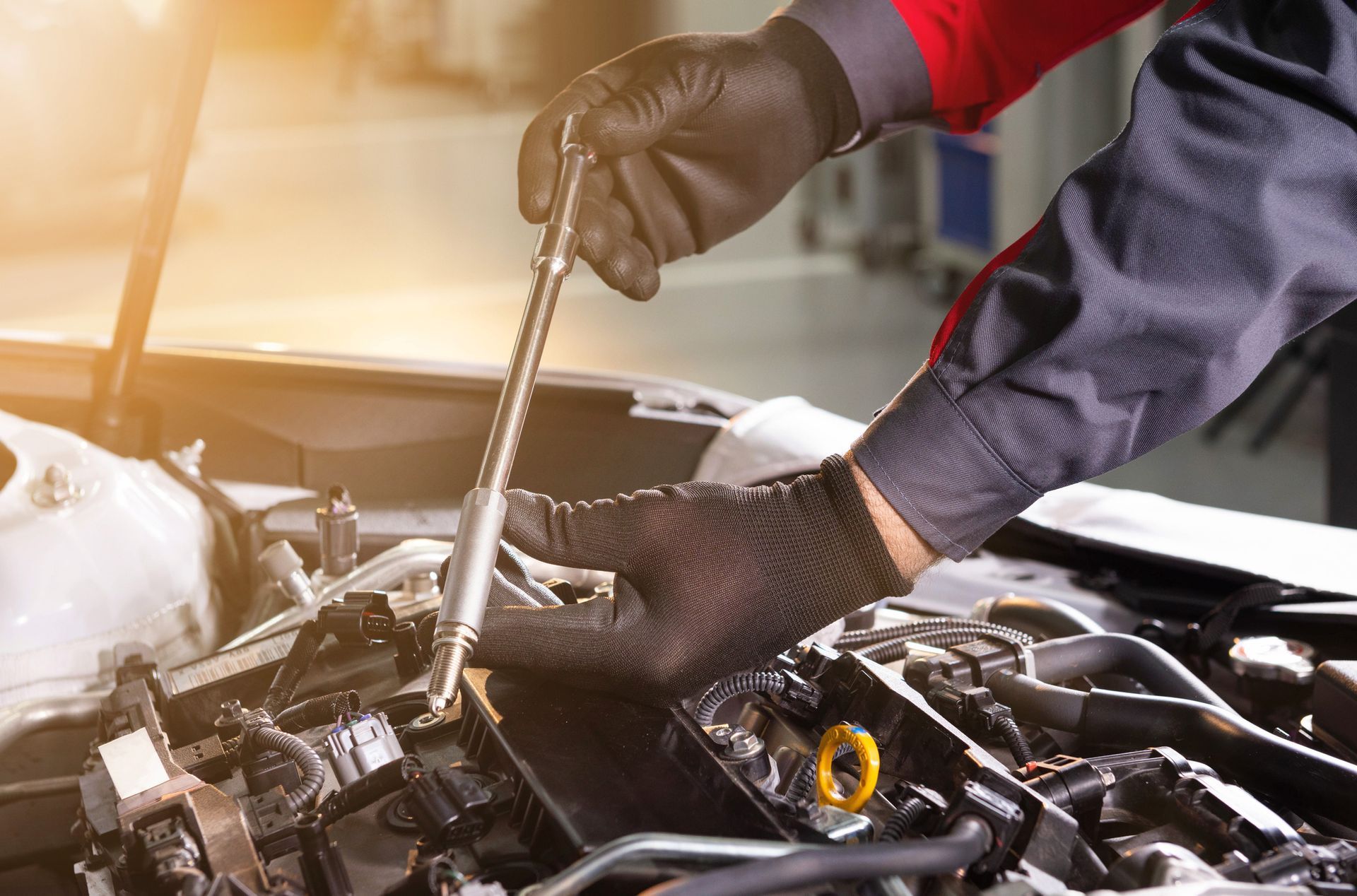 Mechanic in black gloves working on a car engine with a wrench. Bright, indoor setting.