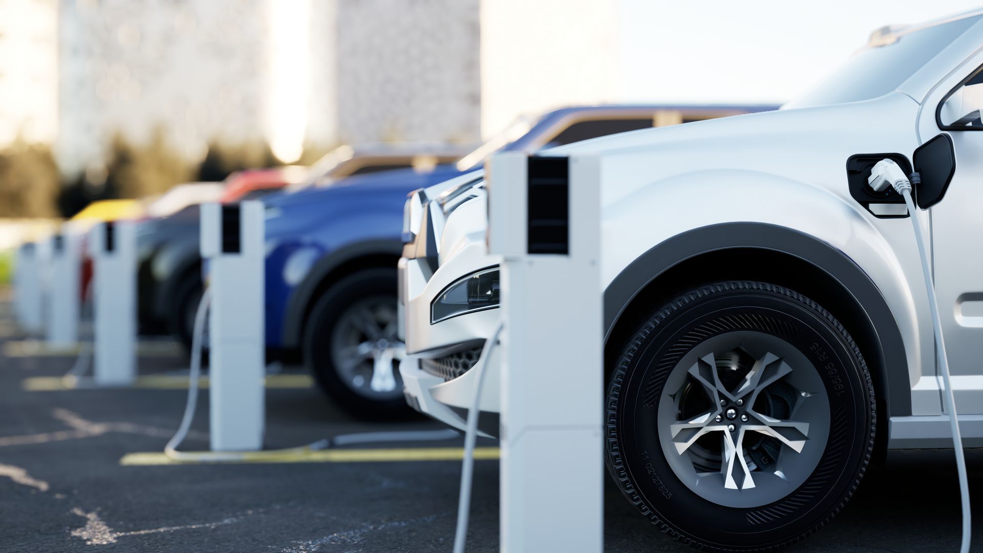 Electric vehicles charging at a station. Silver, blue, and black cars are connected to charging cables.