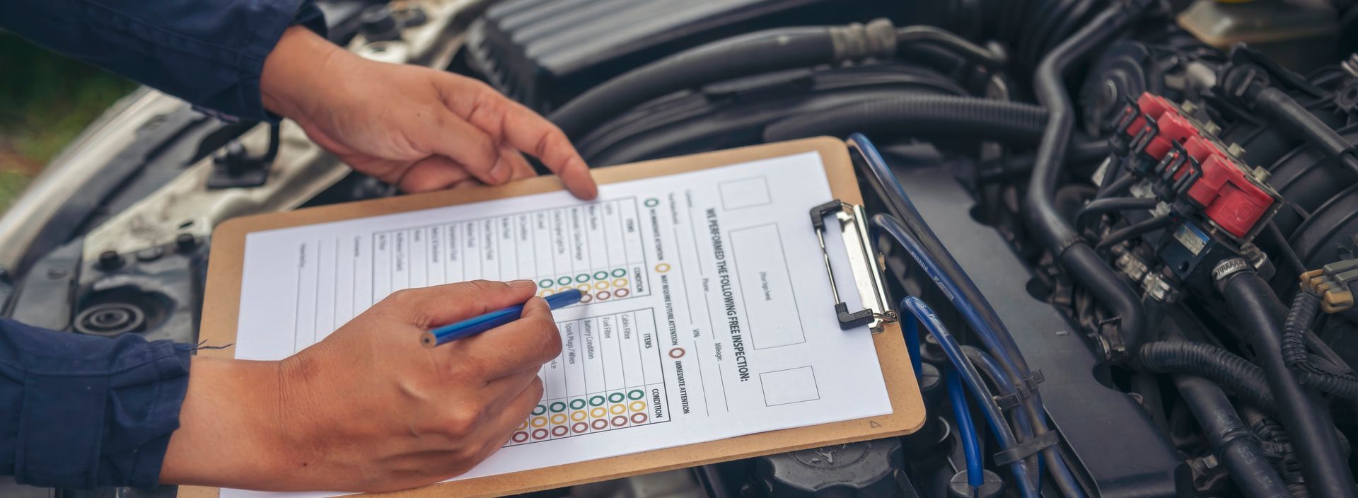 A person filling out a clipboard with a pen in front of a car engine.