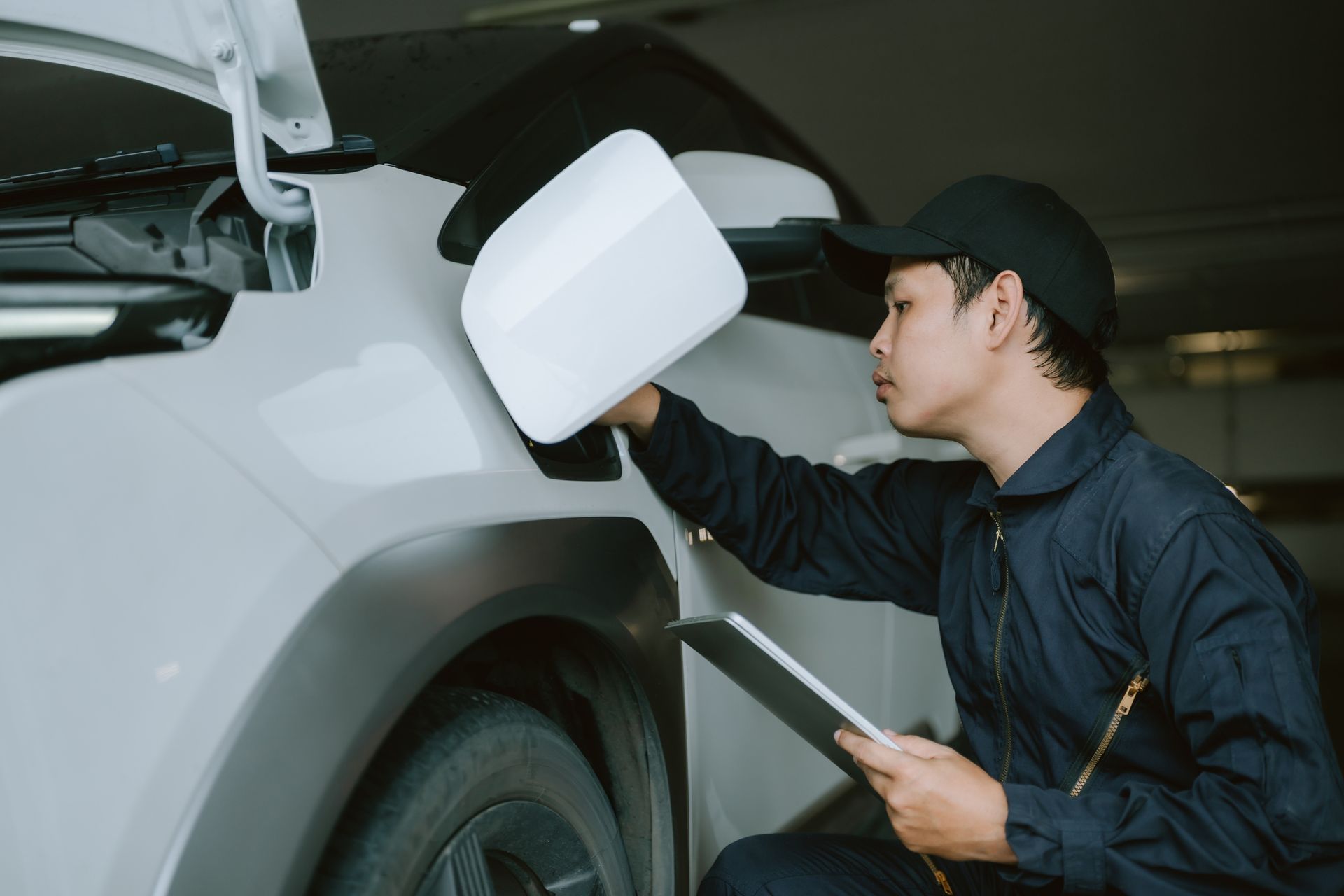 Mechanic inspecting car mirror, holding clipboard, in a garage.