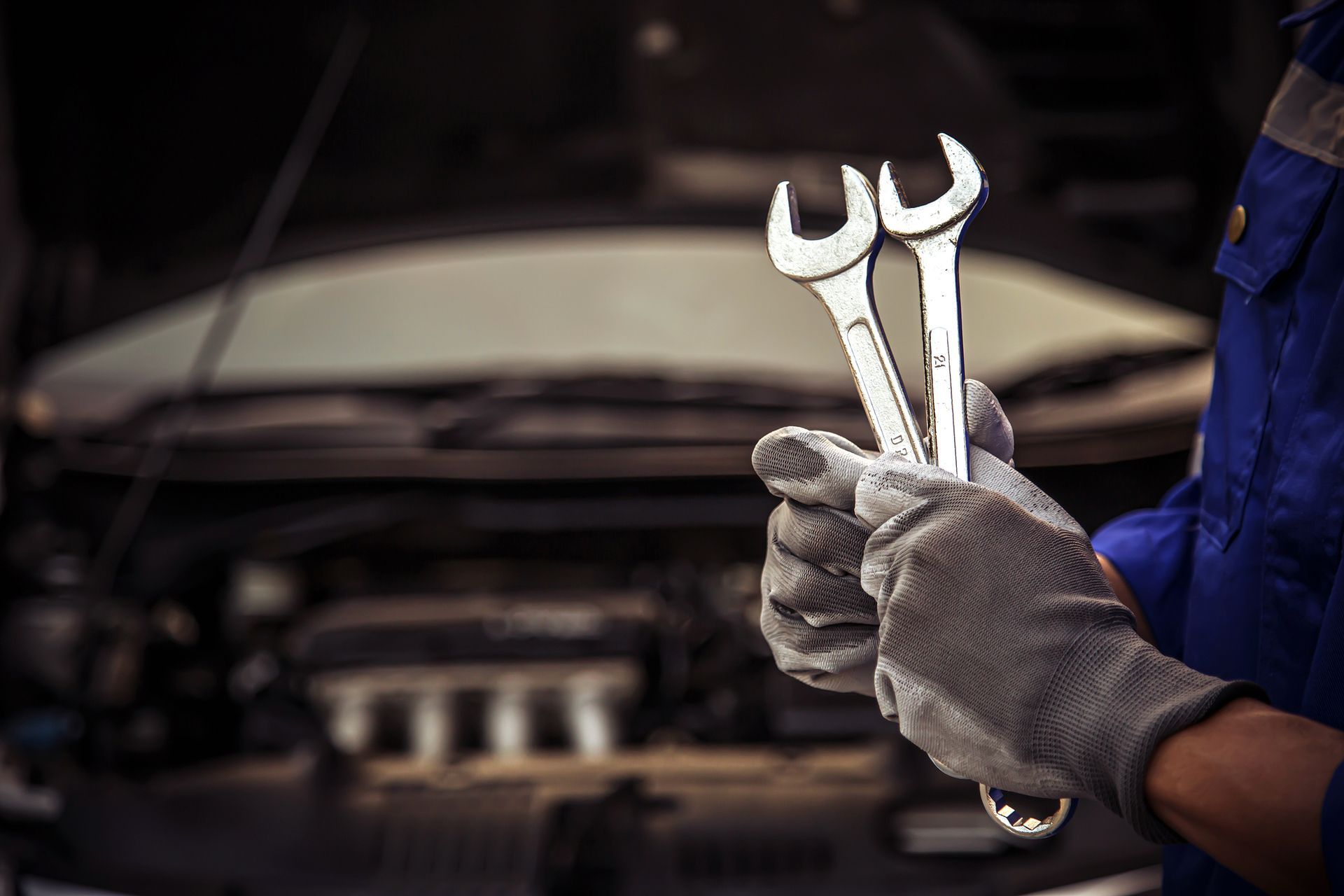 Mechanic holding wrenches near car engine. Wearing gloves and blue work suit. Mechanic holding wrenches near car engine. Wearing gloves and blue work suit.