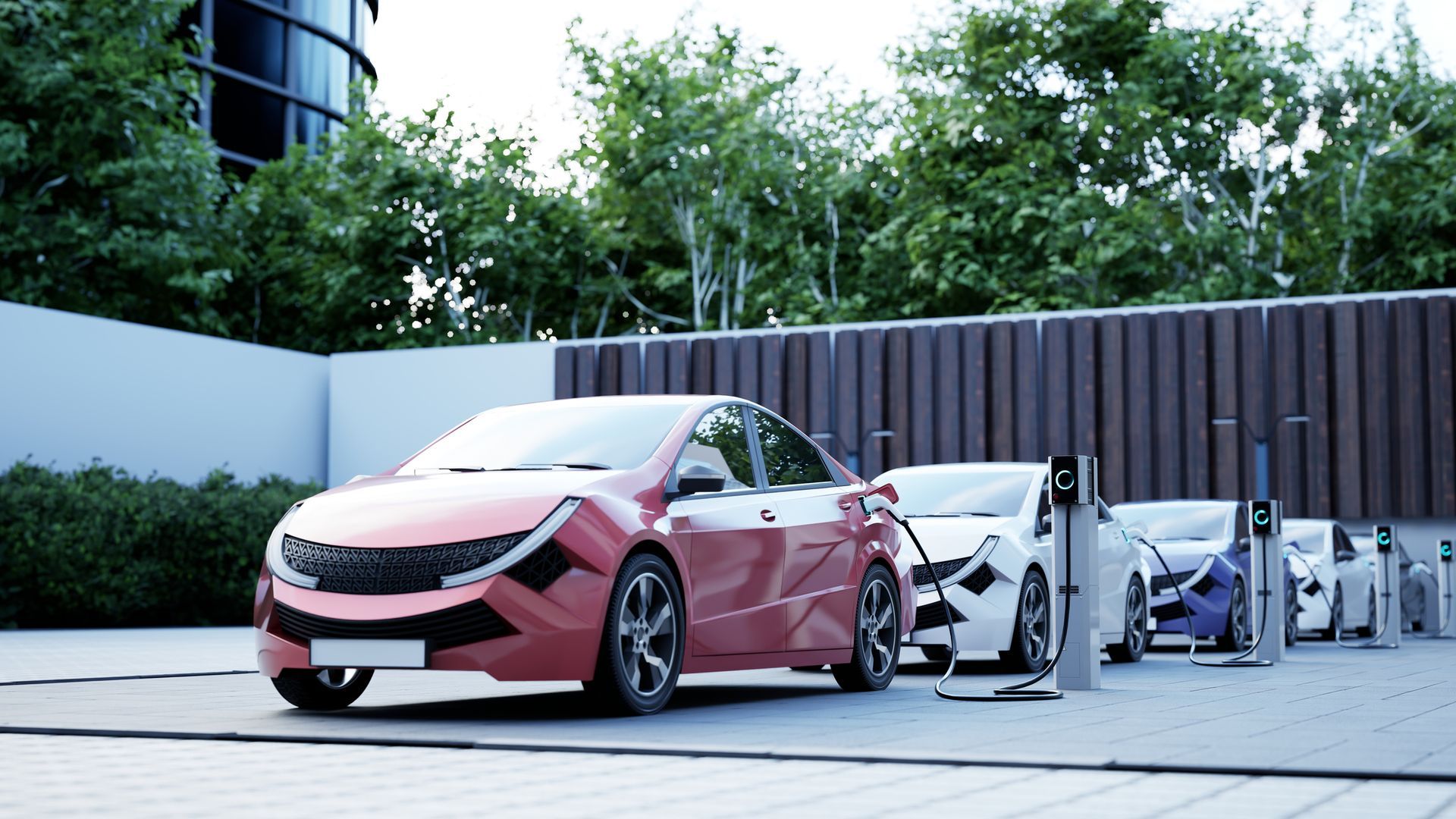 Electric cars charging in a row, with a red car in front. Lush greenery and modern building in the background.