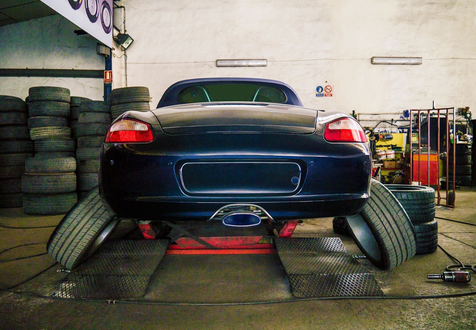Blue Porsche sports car on a lift, tires stacked in a garage. Blue Porsche sports car on a lift, tires stacked in a garage.