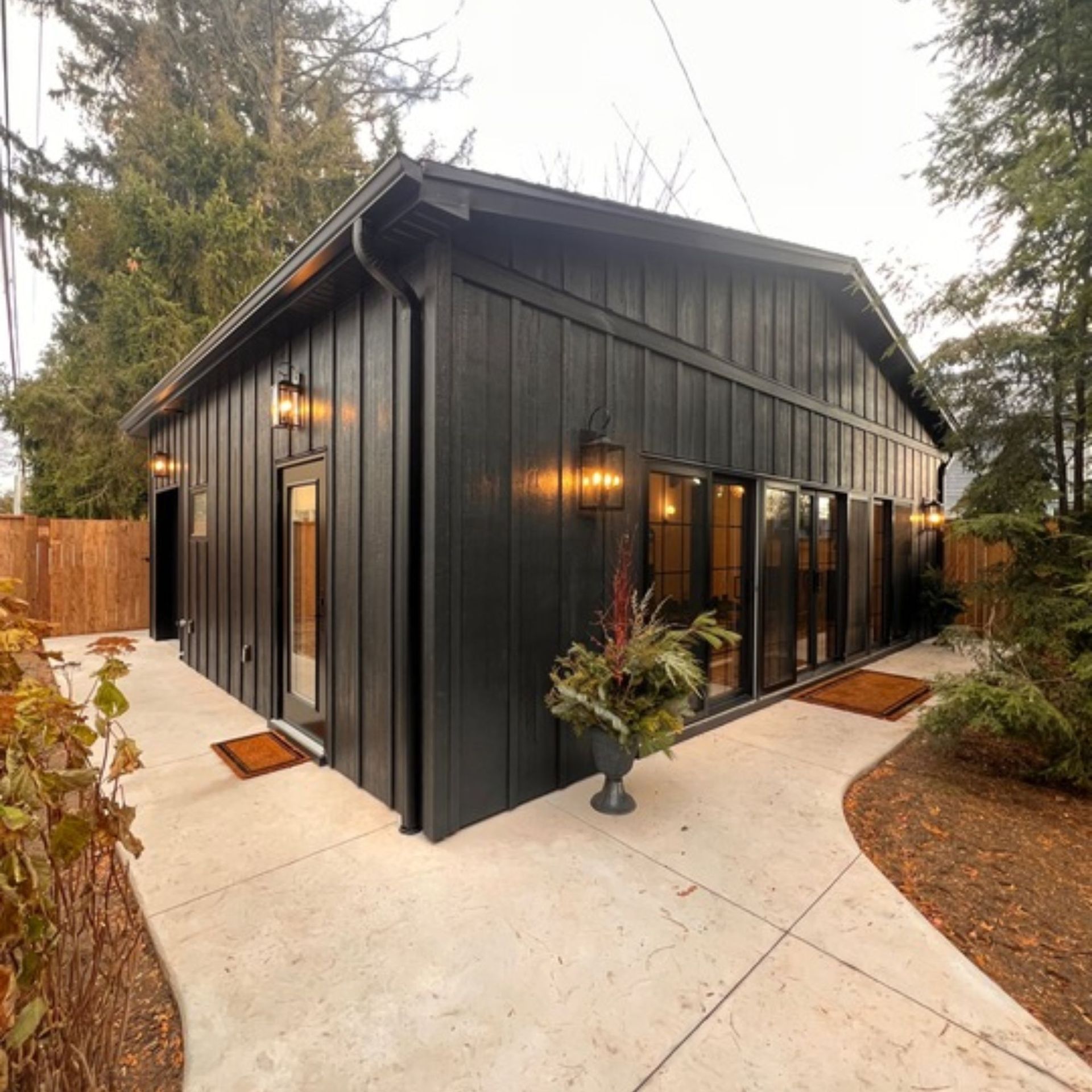 Black-sided modern building with large windows, outdoor lights, and concrete path.