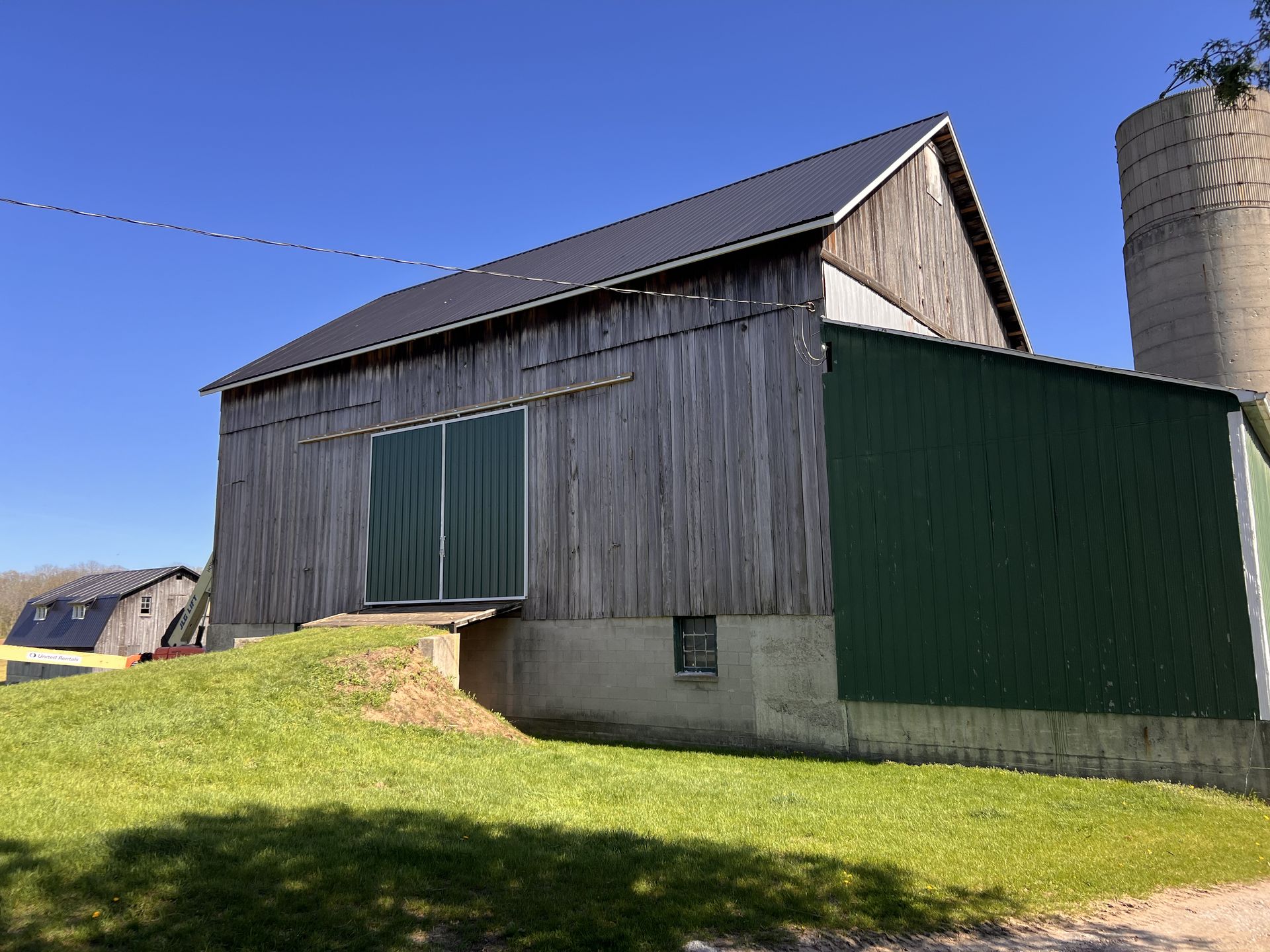 A large wooden barn with a green silo in the background.