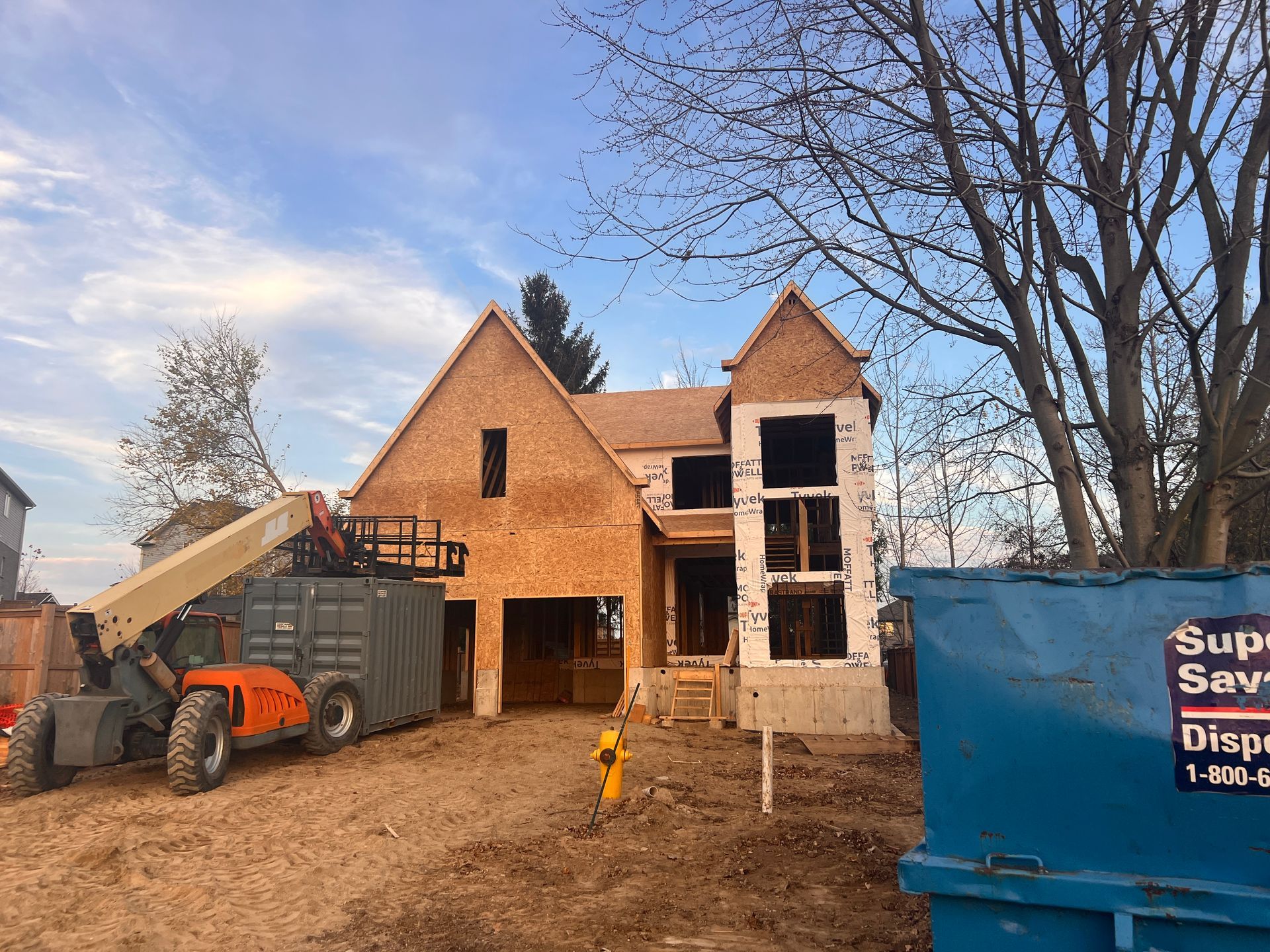 A large house is being built with a dumpster in front of it.