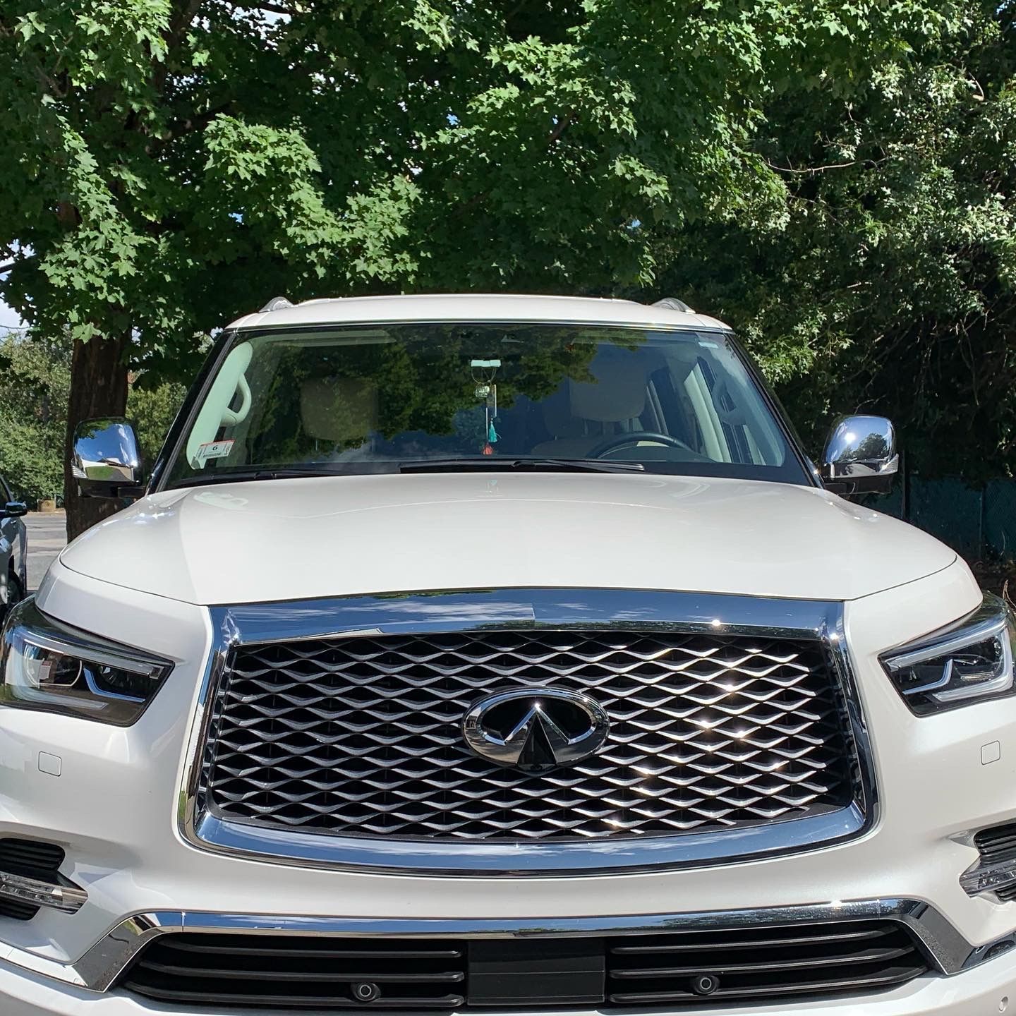 A white infiniti qx80 is parked in front of a tree.