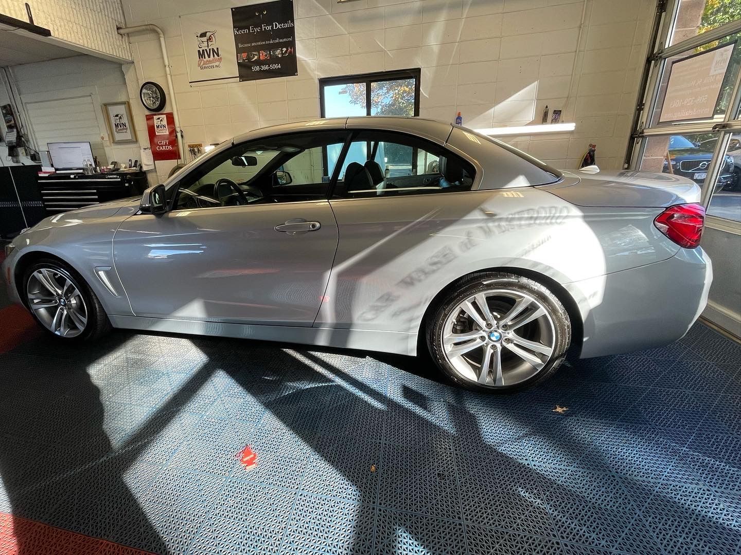 A silver bmw 3 series convertible is parked in a garage.