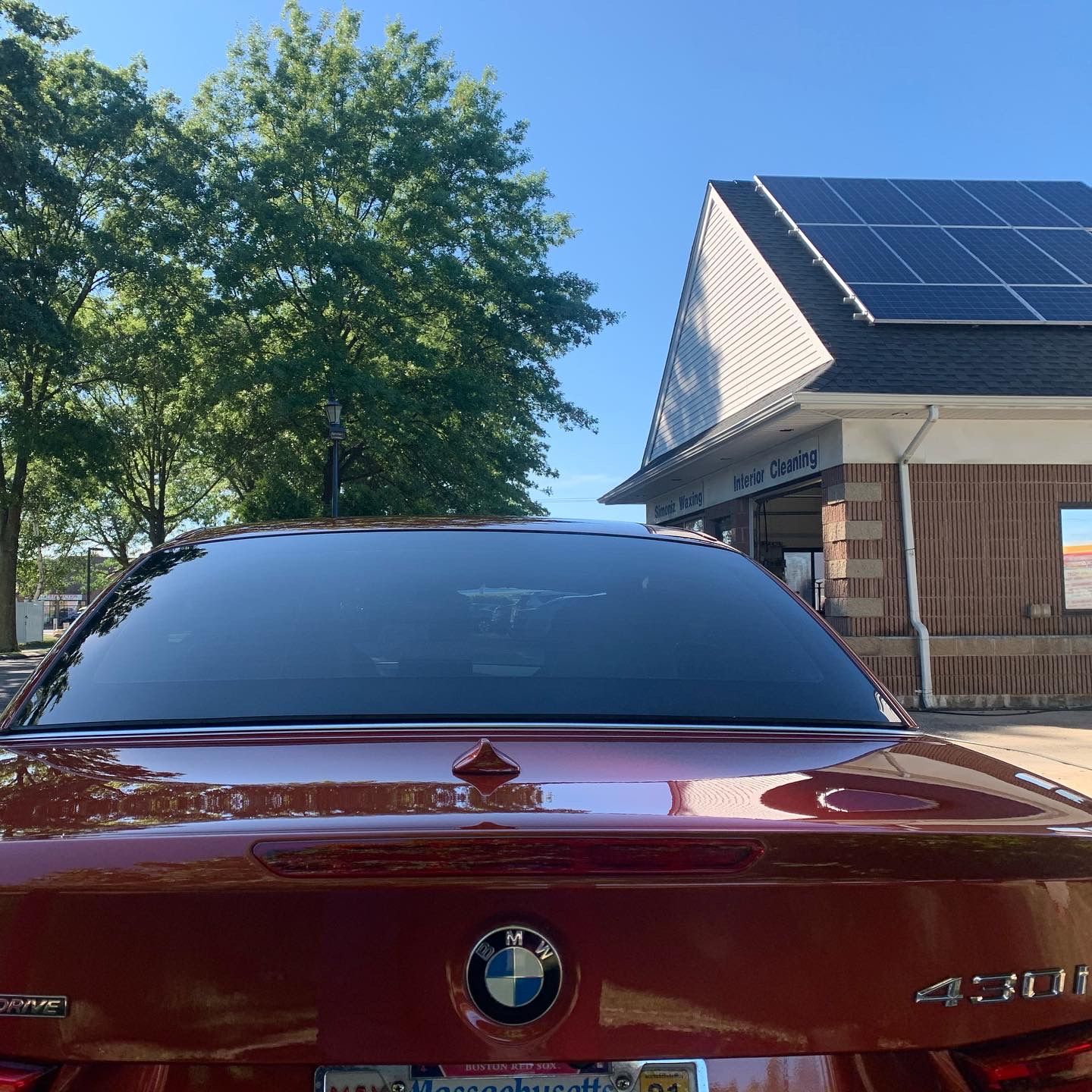 A red bmw is parked in front of a building with solar panels on the roof