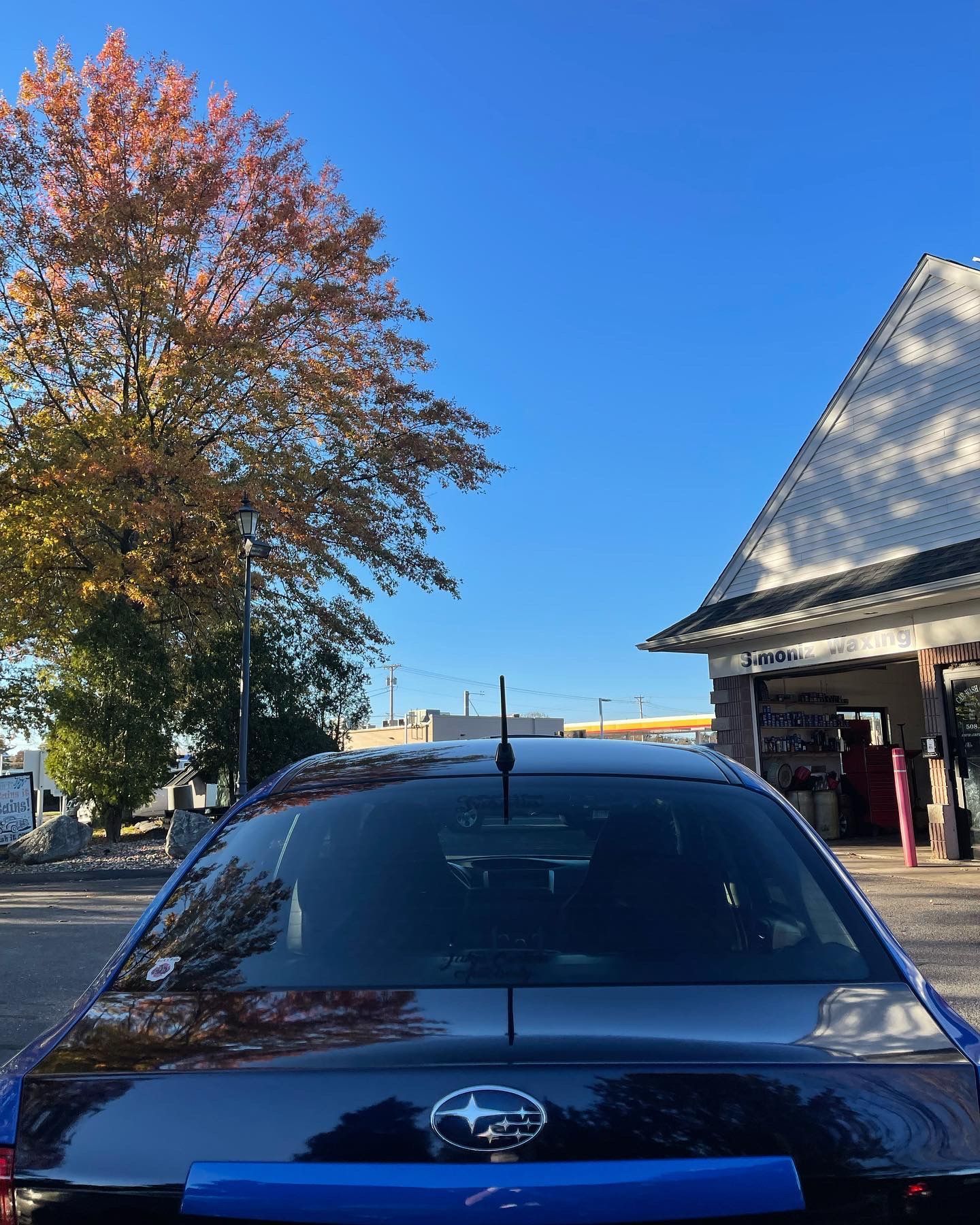 A subaru is parked in front of a garage with a tree in the background.