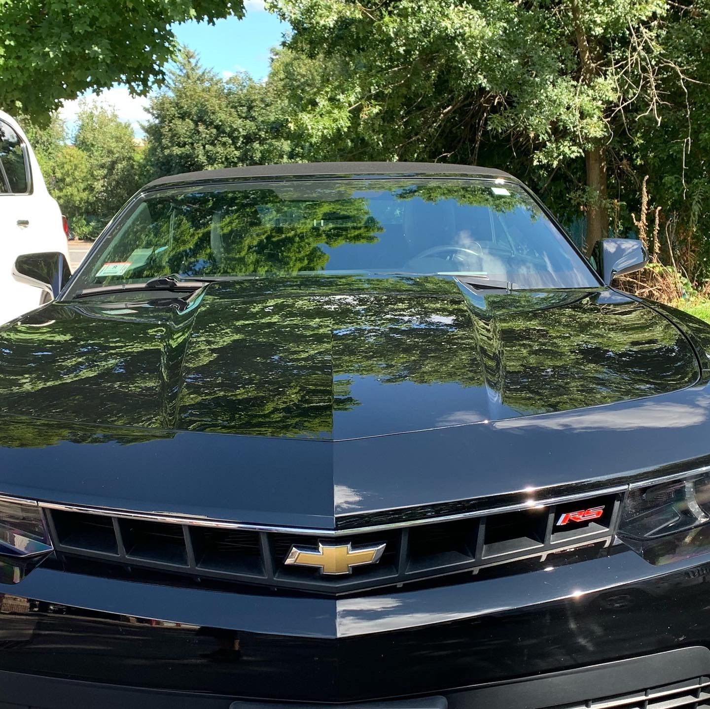 A black chevrolet camaro is parked in a parking lot with trees in the background.