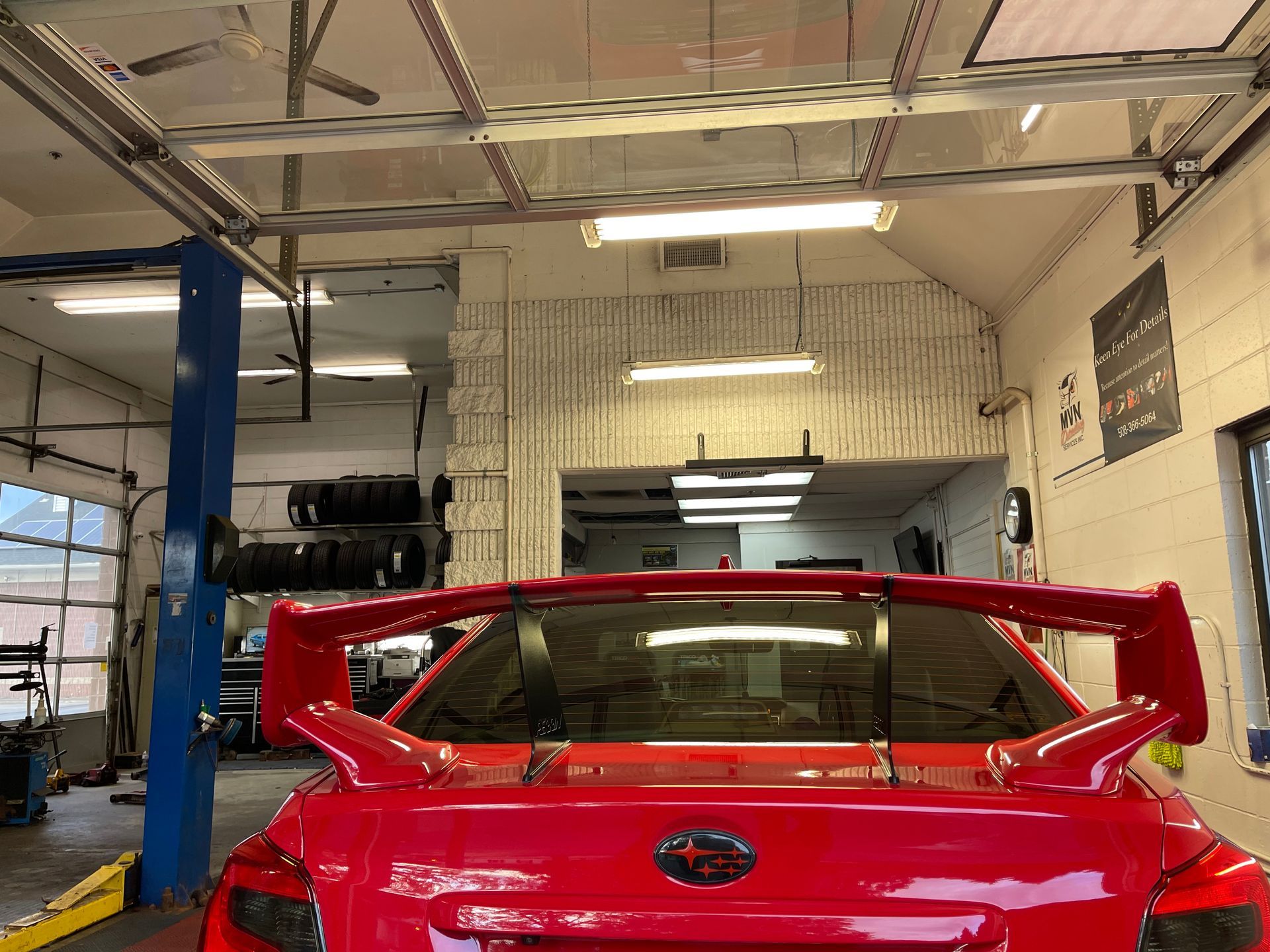 A red car with a spoiler on the back is parked in a garage.