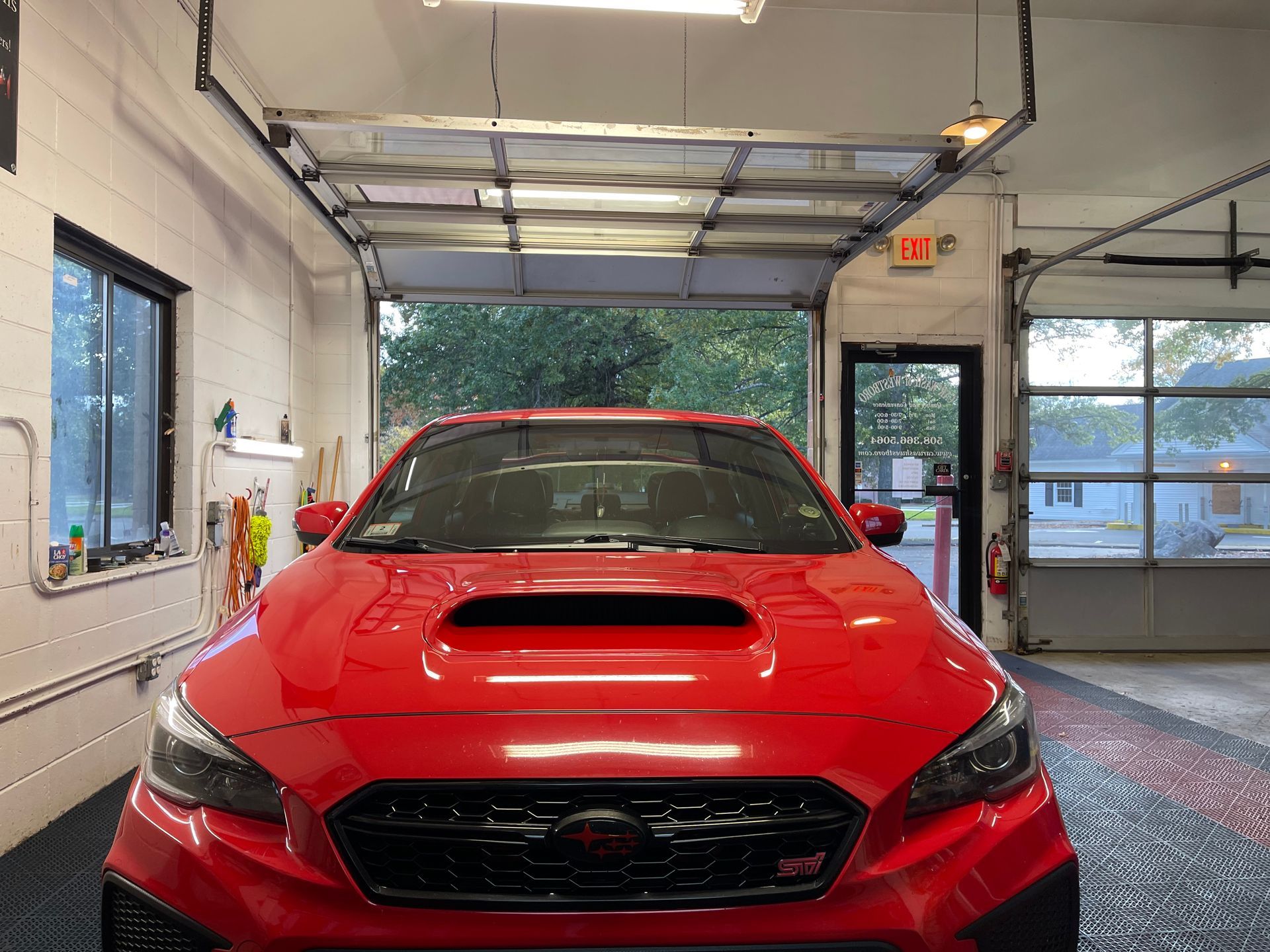 A red car is parked in a garage with a garage door open.