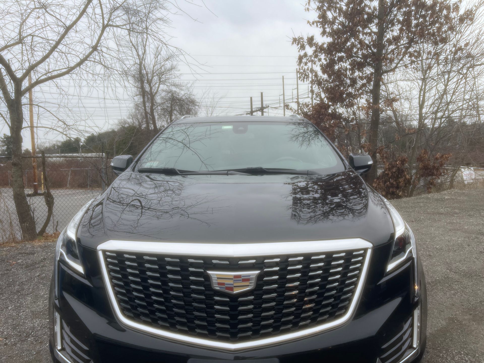 A black cadillac is parked in a parking lot with trees in the background.