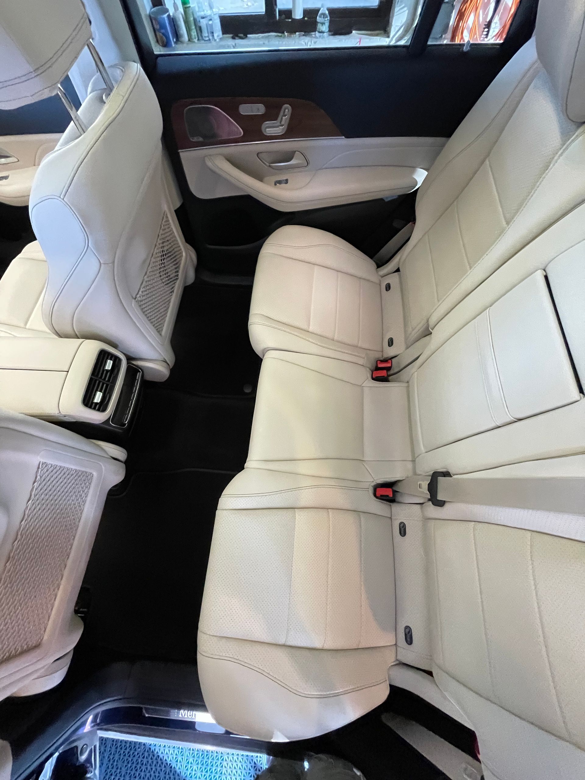 The rear seats of a car are white and have a red seat belt.