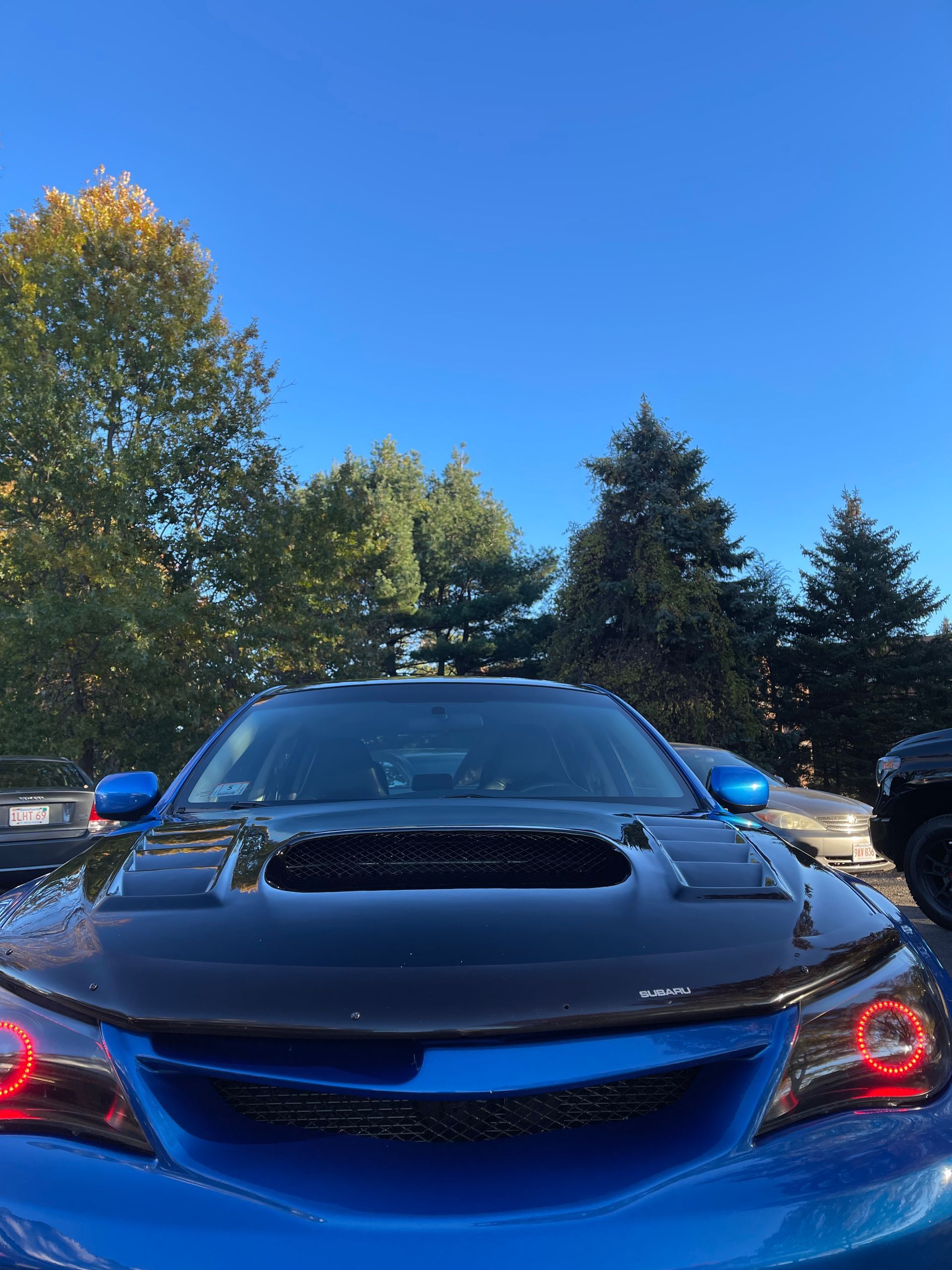 A blue car is parked in a parking lot with trees in the background.