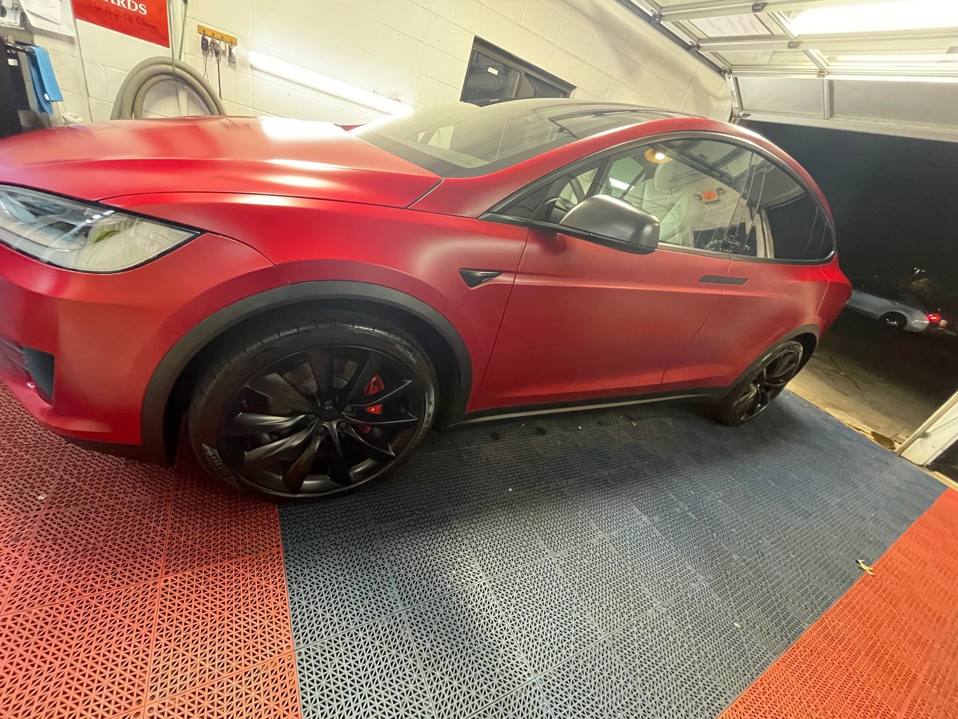 A red tesla model x is parked in a garage.