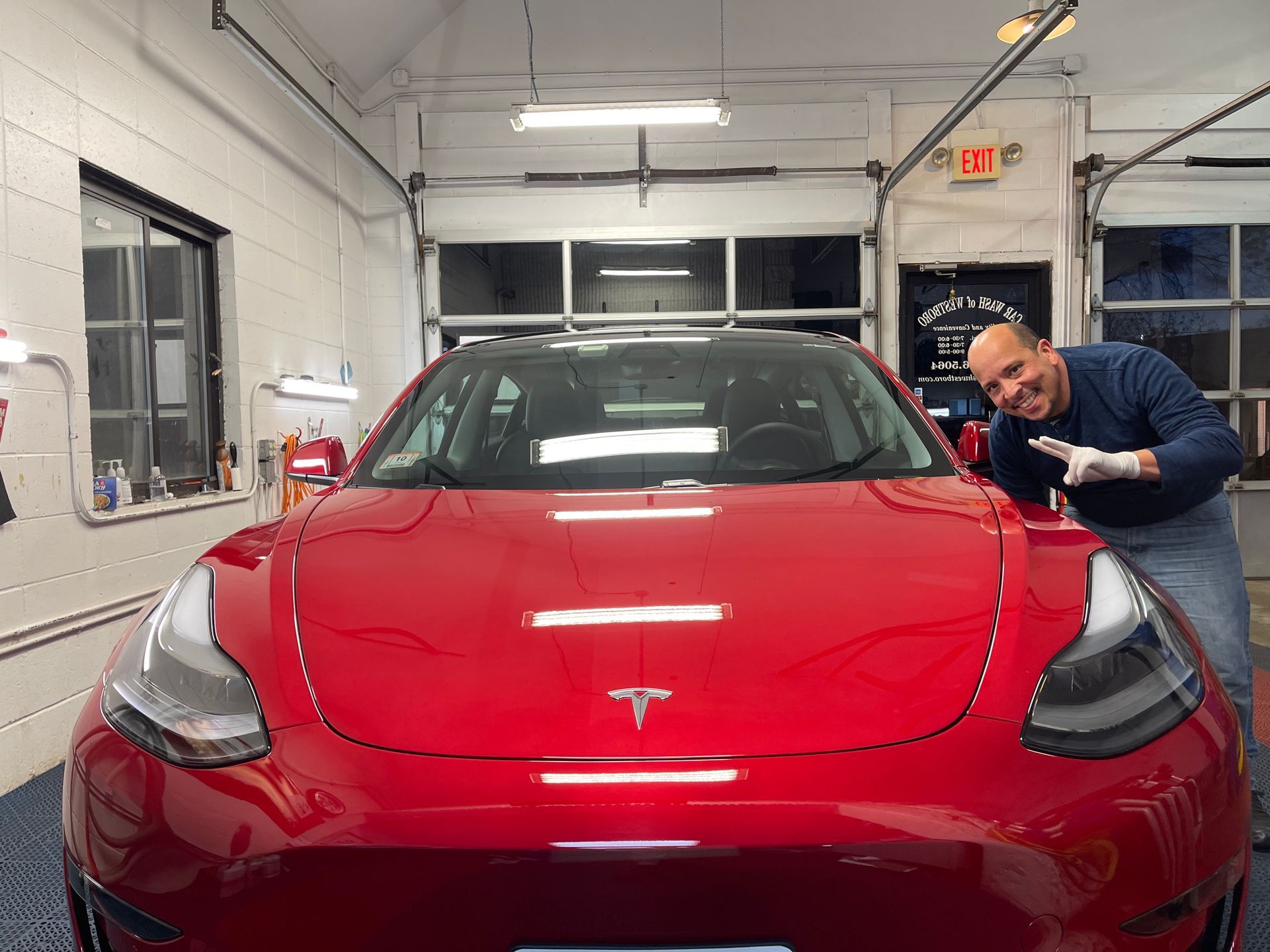 A man is standing in front of a red tesla model 3 in a garage.