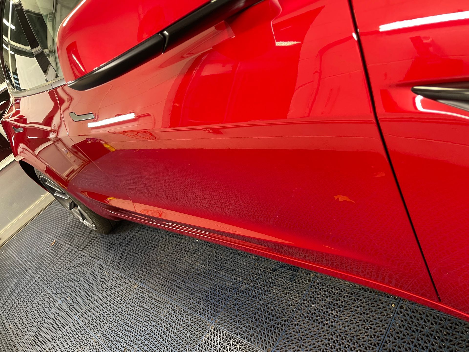 A red car is parked in a garage on a tiled floor.
