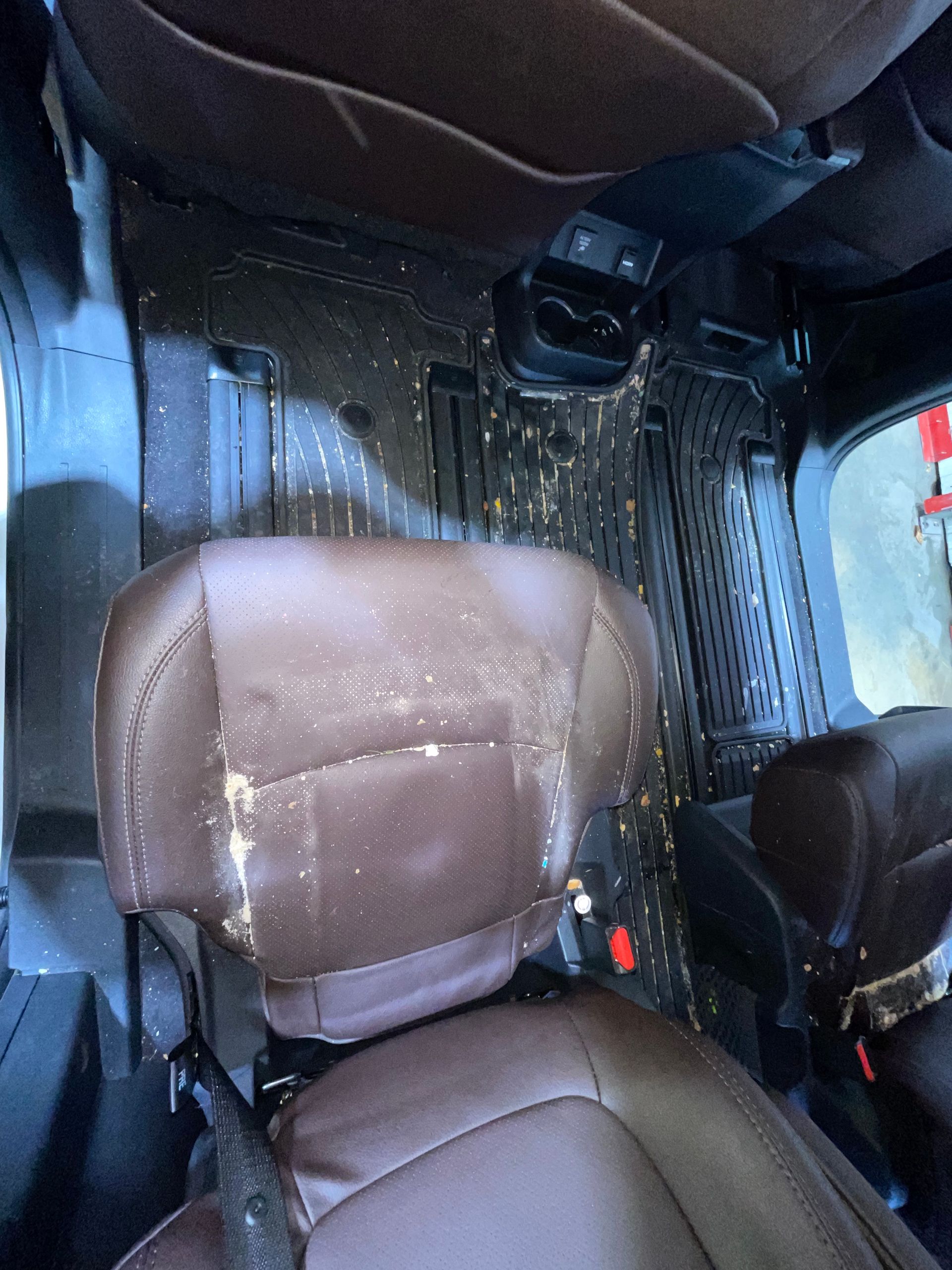 A brown leather seat in a car with a dirty floor