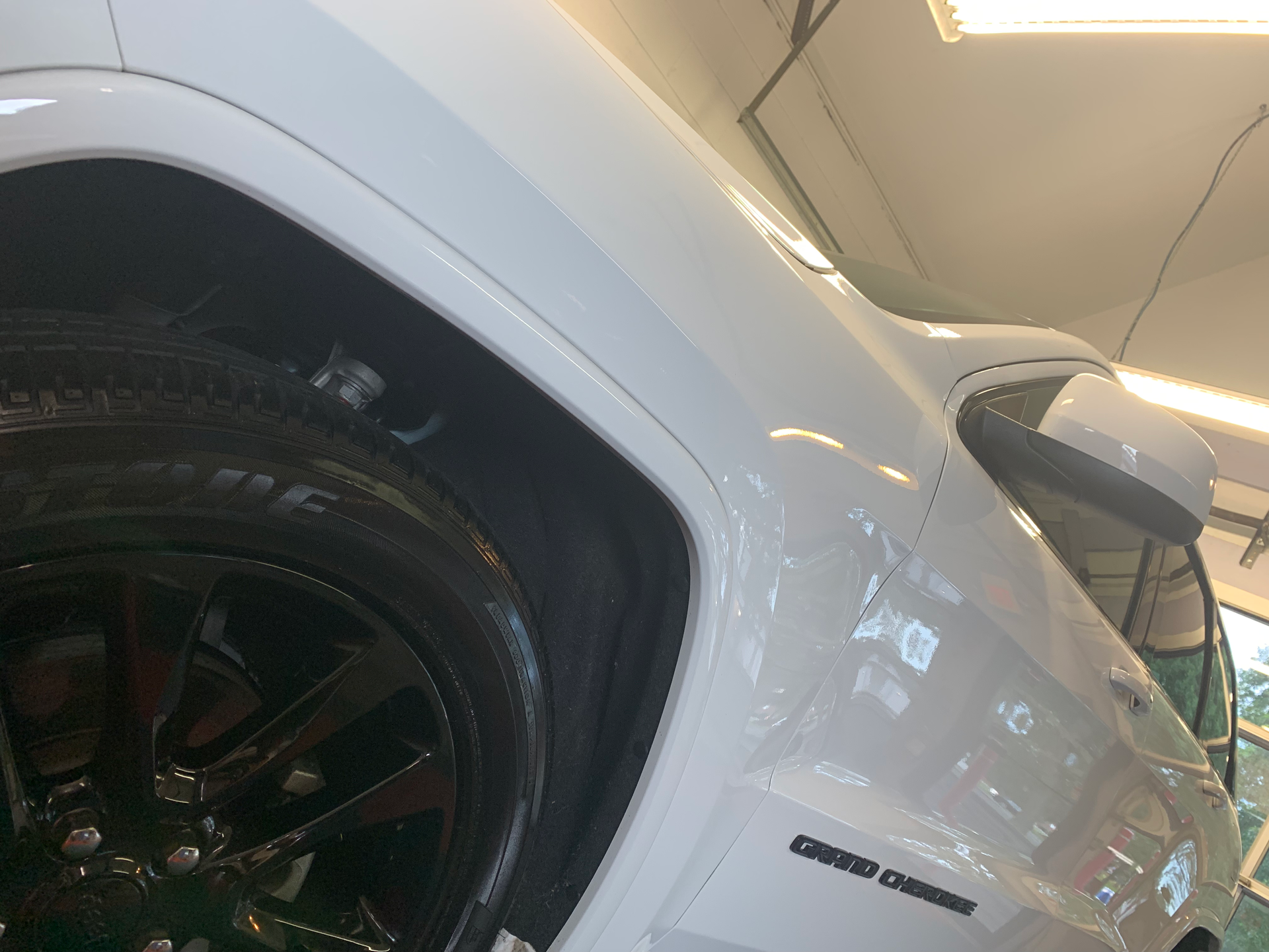 A white car with black wheels is parked in a garage.