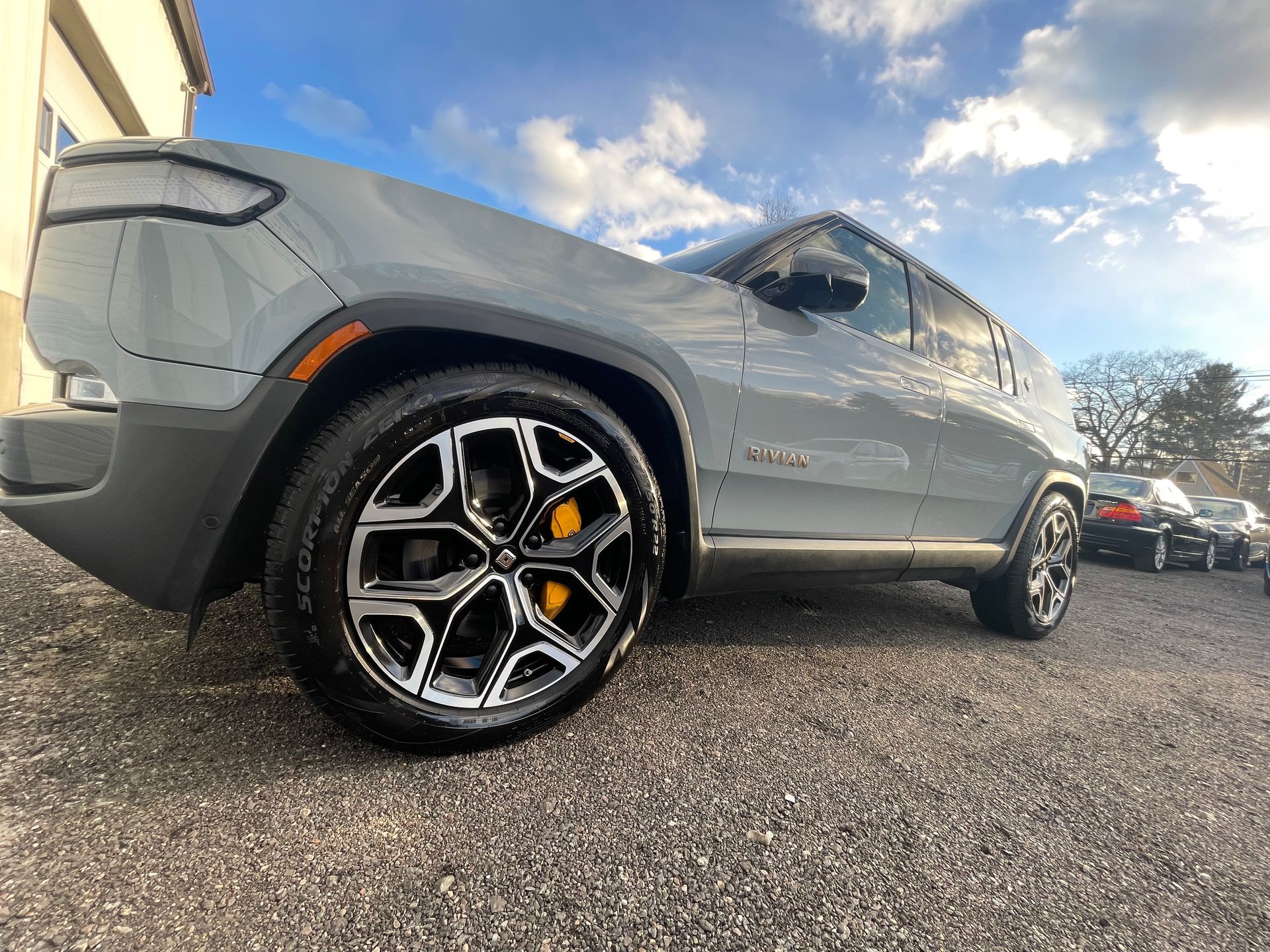 A gray jeep is parked in a gravel lot.