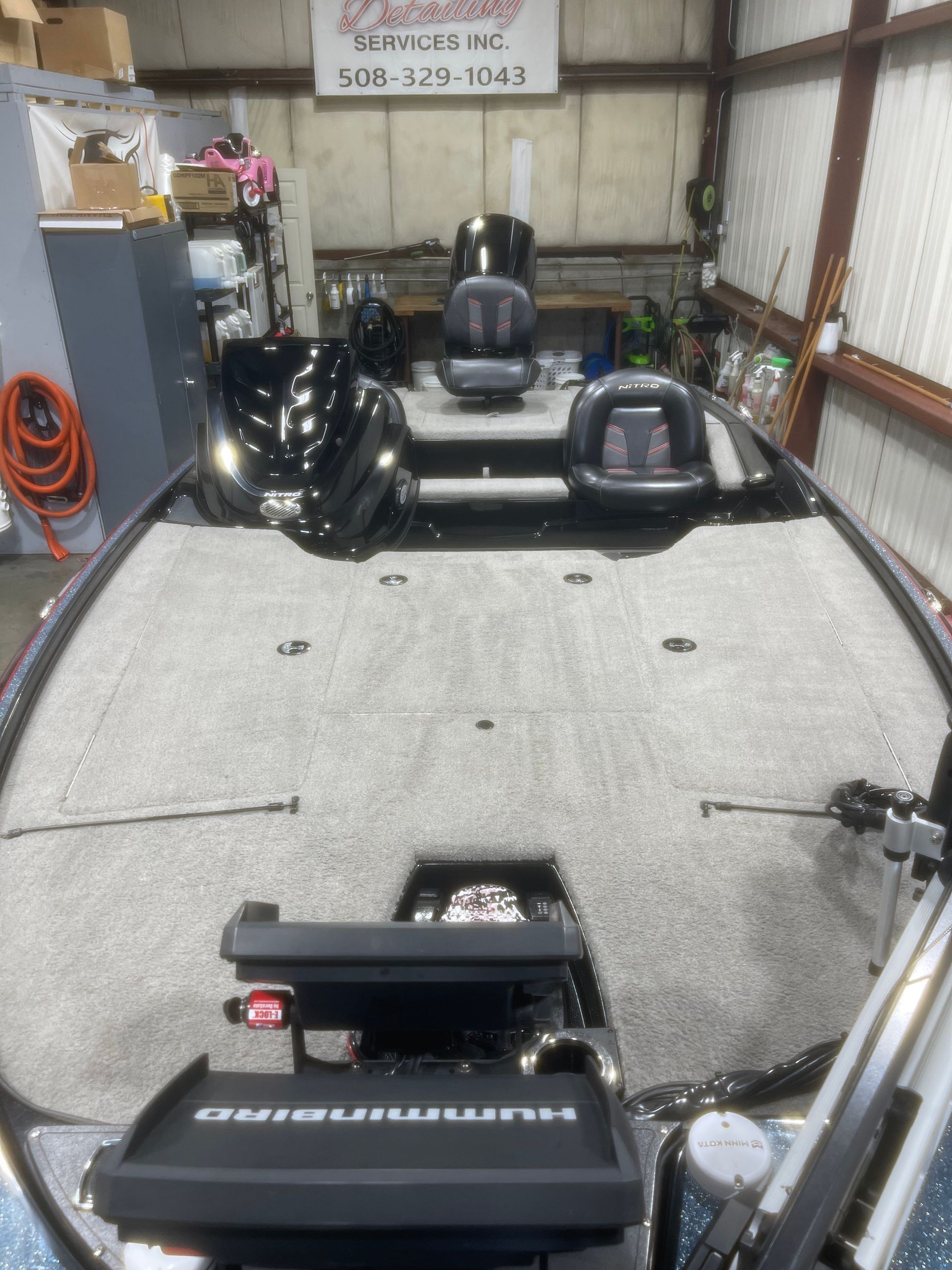 A fishing boat is sitting in a garage next to a sign that says detailing services