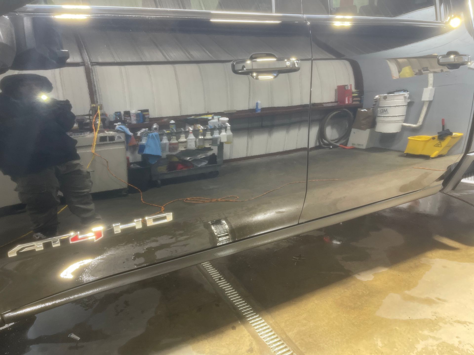 A man is standing next to a black truck in a garage.